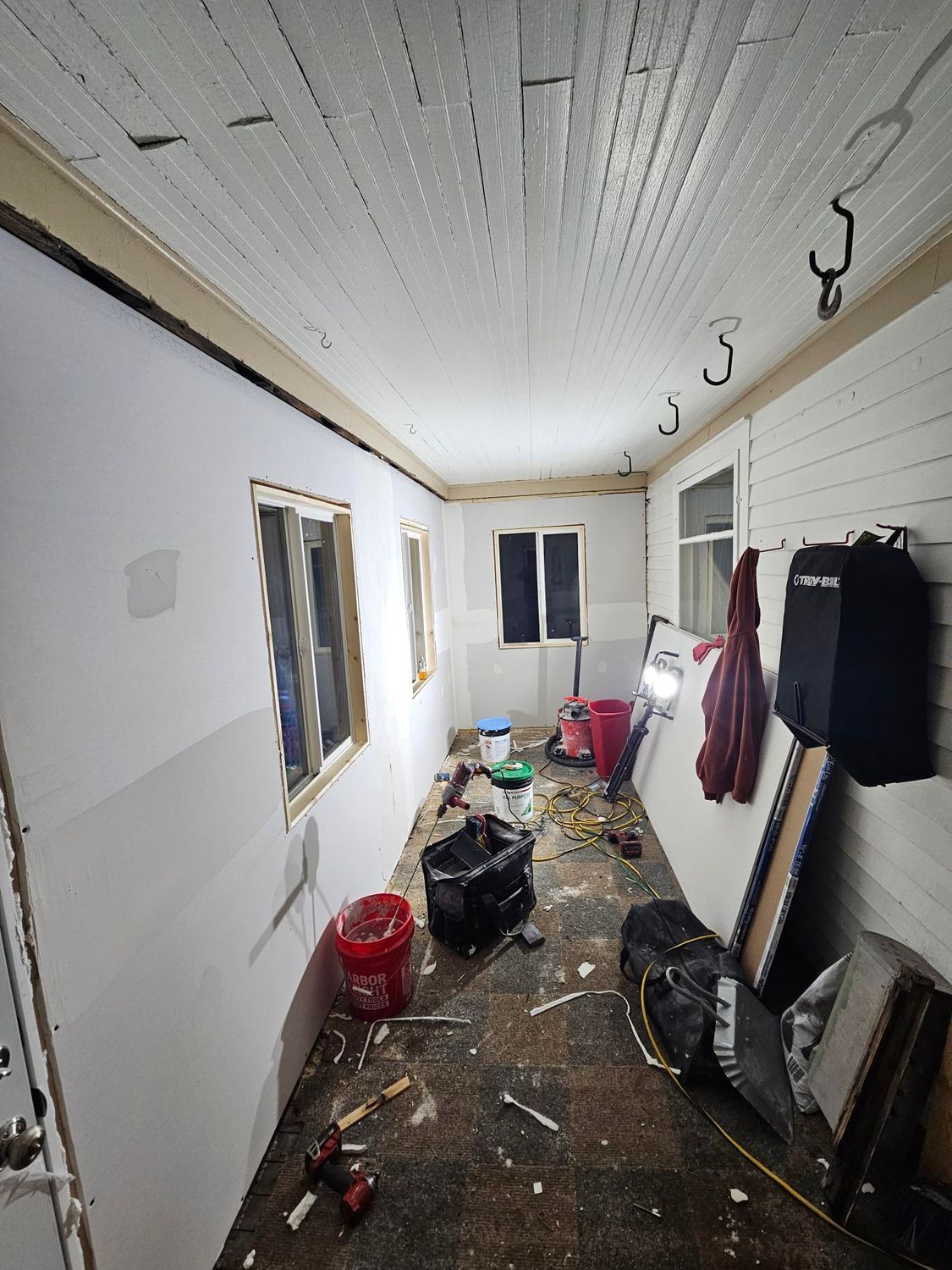 Narrow unfinished hallway with clutter, hanging coats, exposed lighting, and debris on the floor.