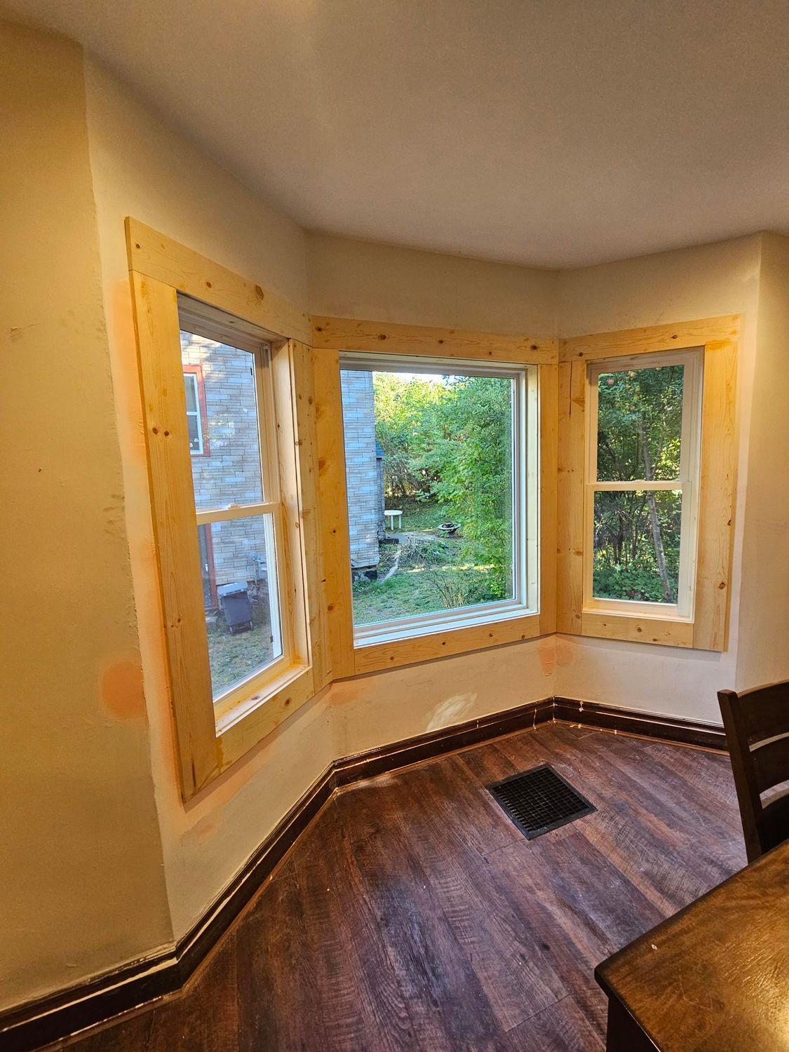 Curved bay windows with unfinished wood trim in a small empty room, showing greenery outside.