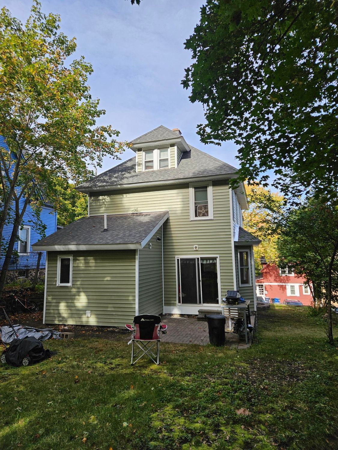 Yellow two-story house with a porch in a leafy yard on a sunny day