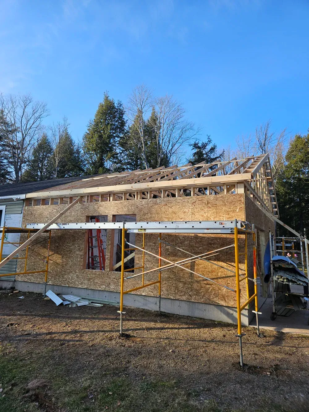 Partially framed house under construction with scaffolding and exposed insulation in a wooded area