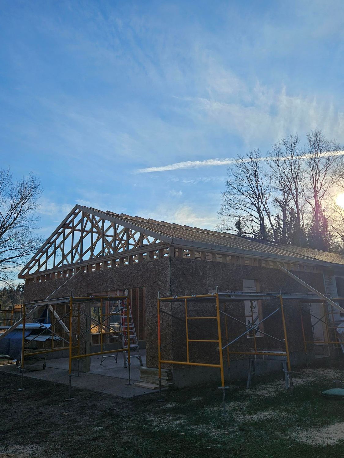 Partially framed house under construction with scaffolding at sunset under a blue sky