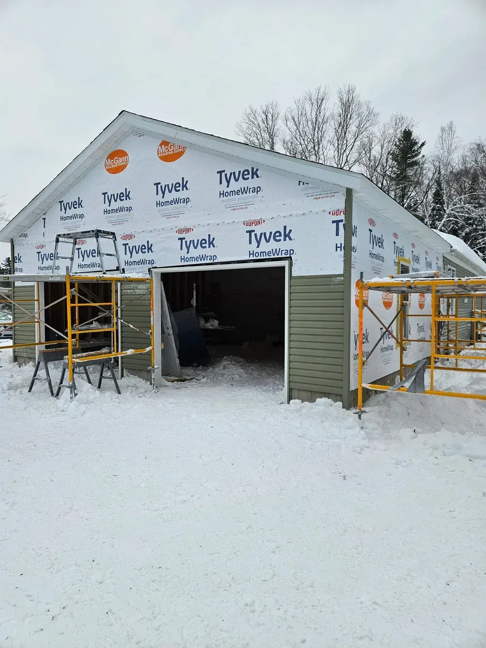 Snow-covered garage under construction with Tyvek wrap and scaffolding around the entrance