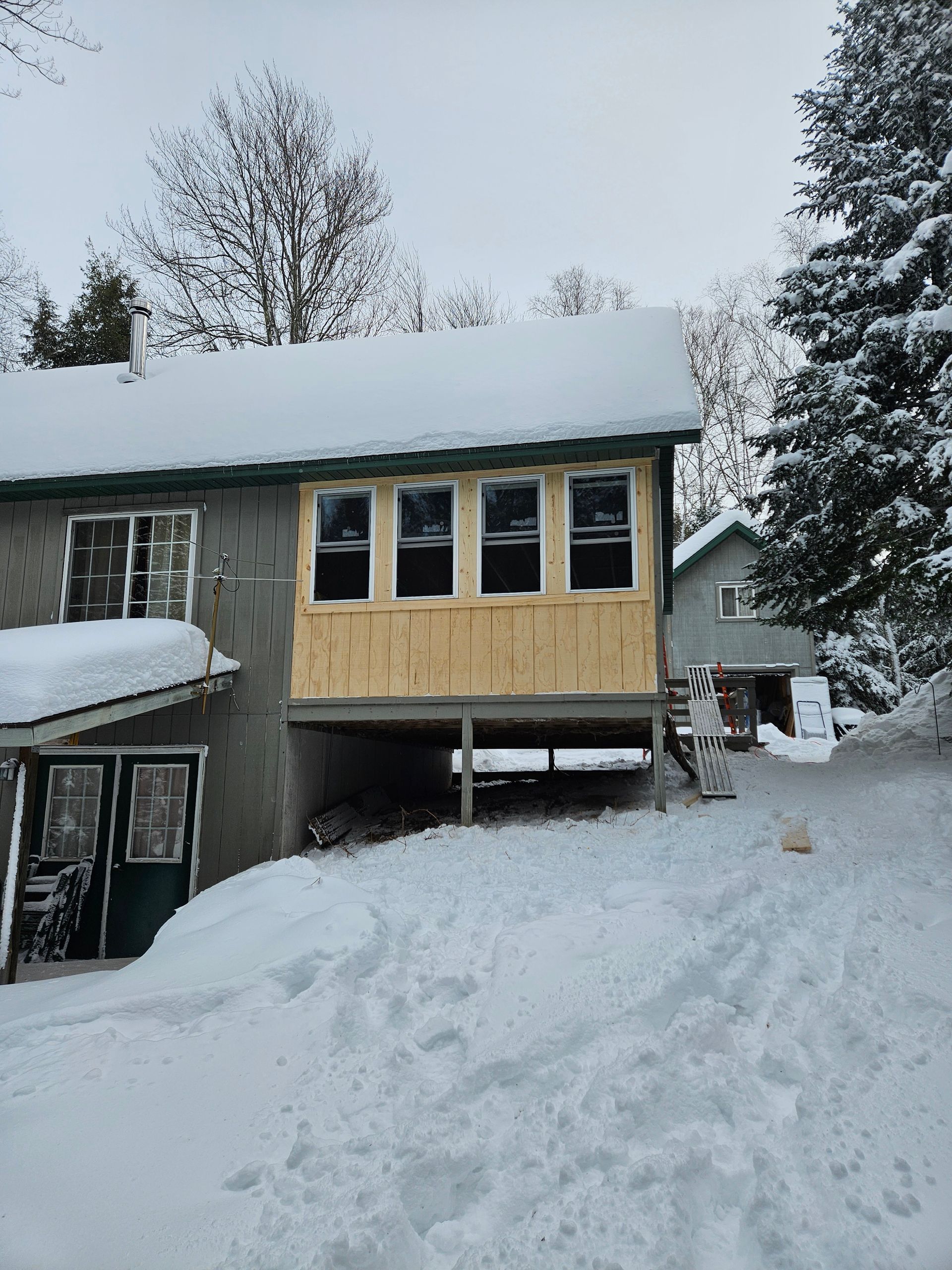 Snow-covered house with a beige upper facade and trees in the background