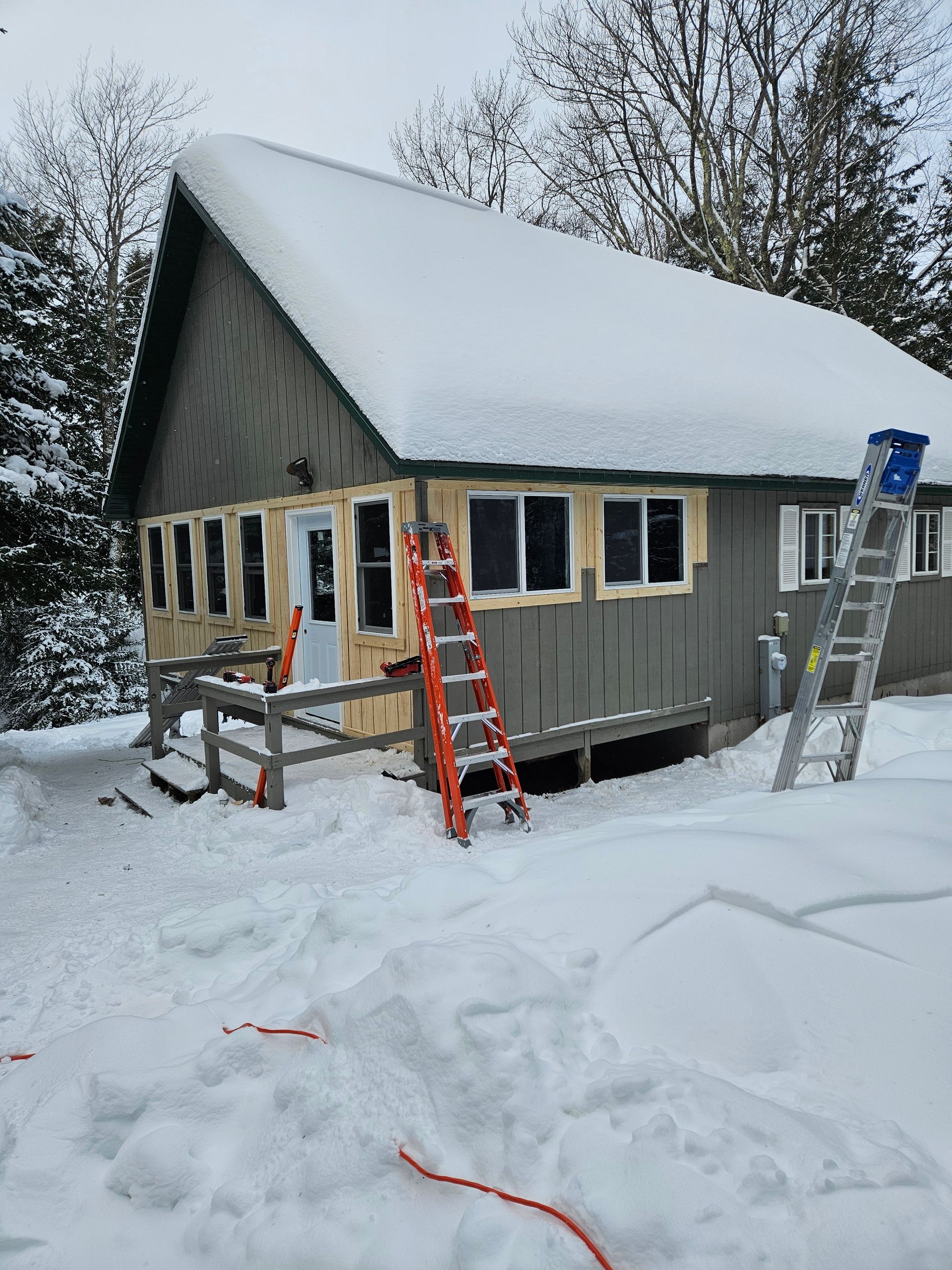 Snow-covered house under construction with ladders and scaffolding in a winter yard