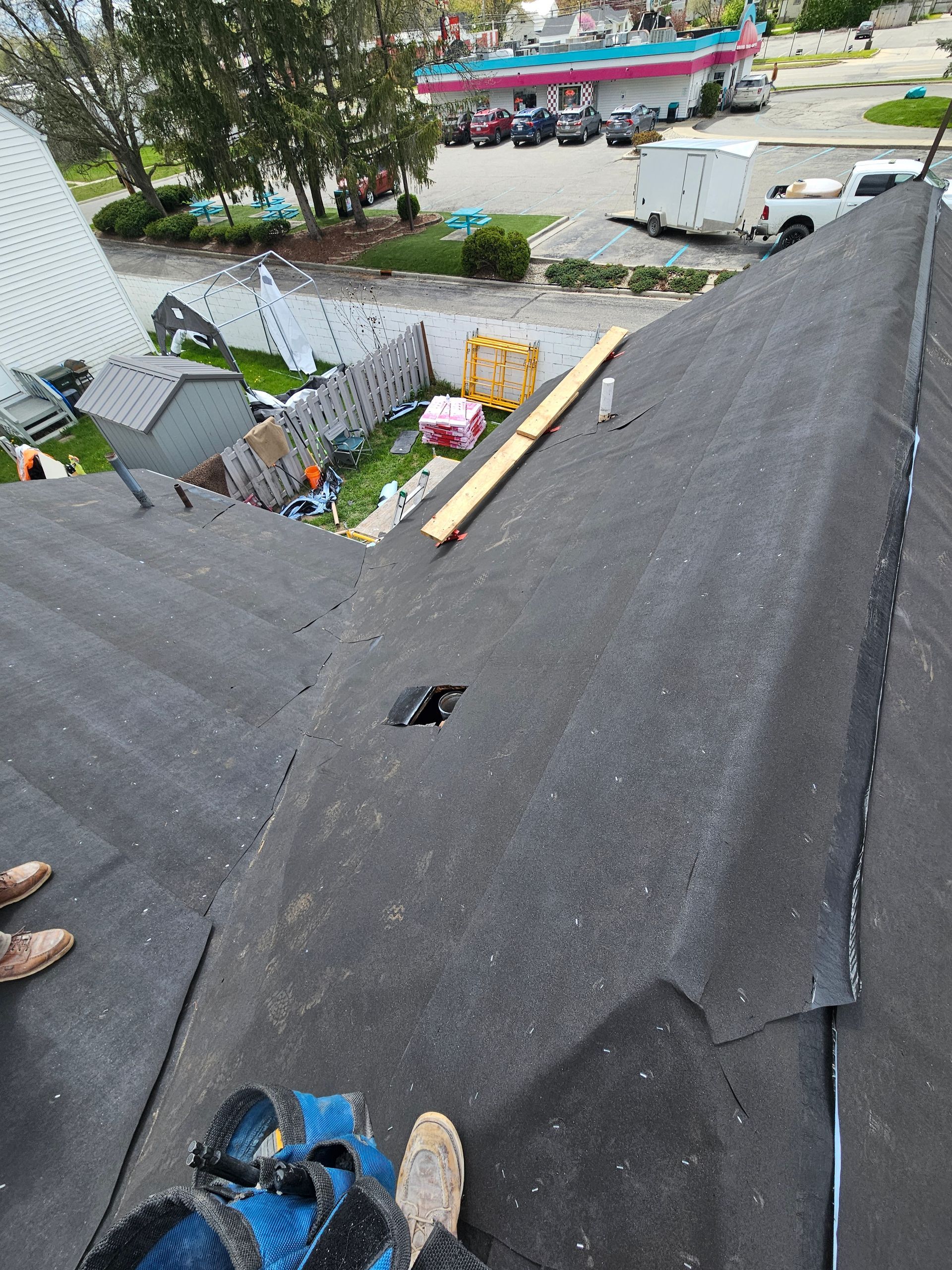 View from a roof with dark shingles, looking down at a backyard and street with a parked white van.