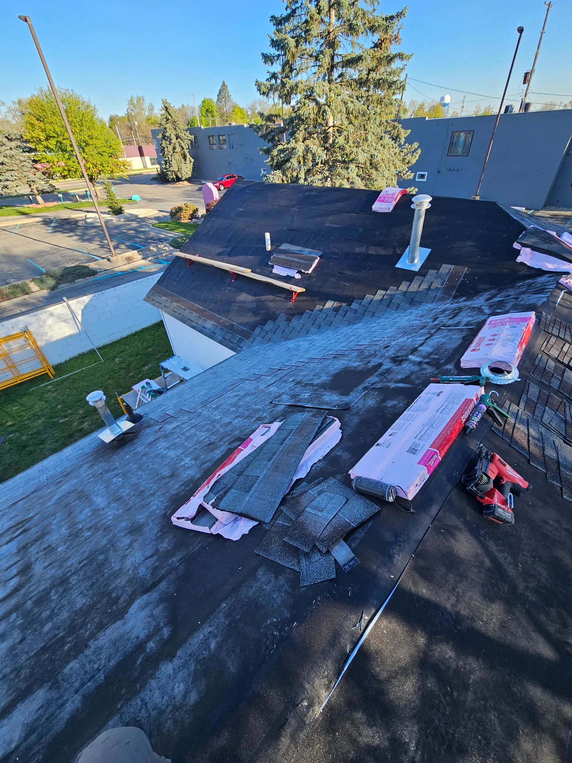 Roof under construction with black roofing felt, insulation boards, and tools on a sunny day