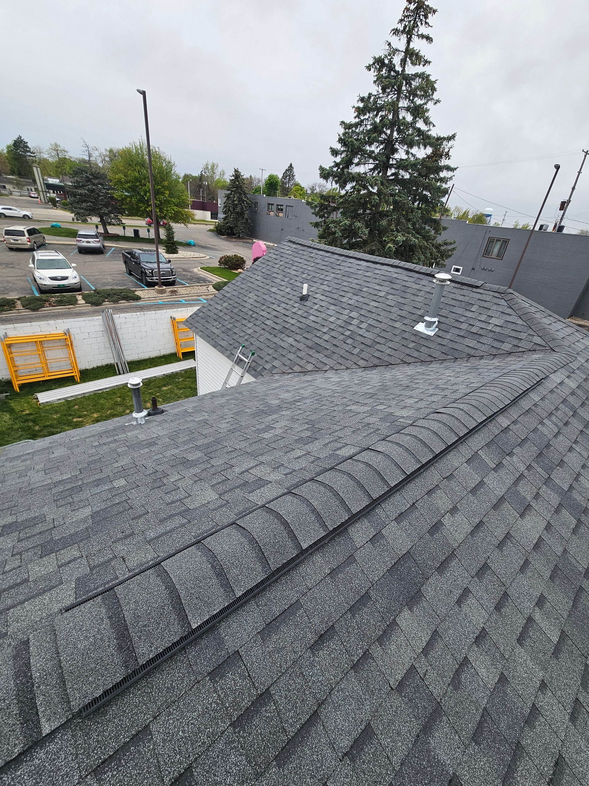 Gray shingled rooftop overlooking a parking lot and trees on an overcast day