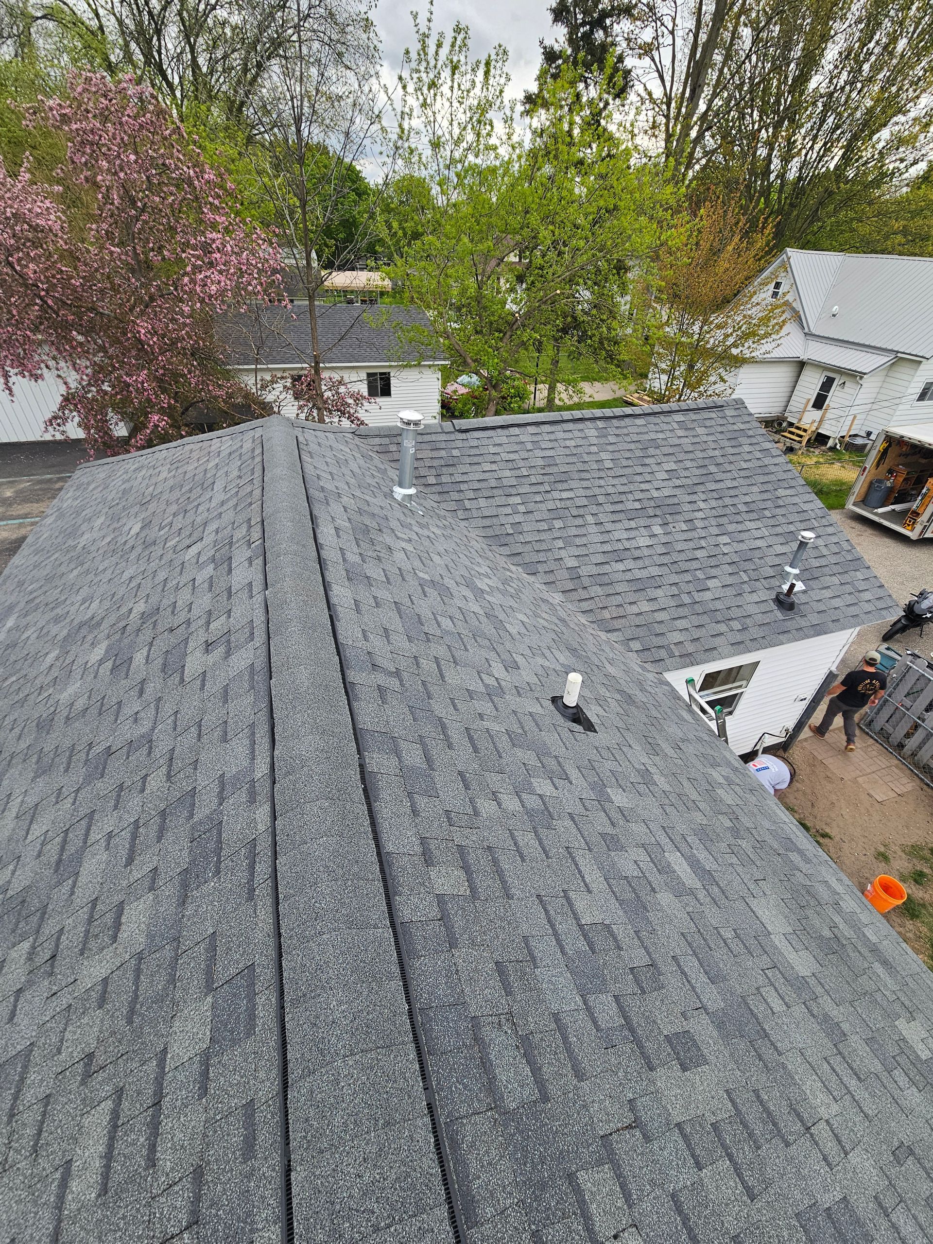 Gray shingled roof with two small white fixtures, overlooking trees and neighboring houses
