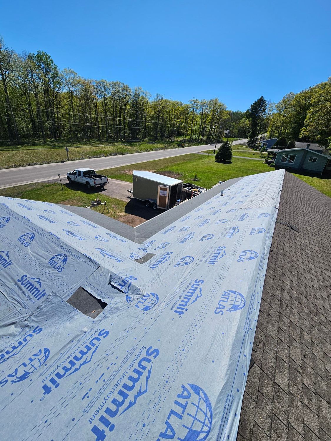 Rooftop view of a worksite with parked vehicles, trees, and a bright blue sky