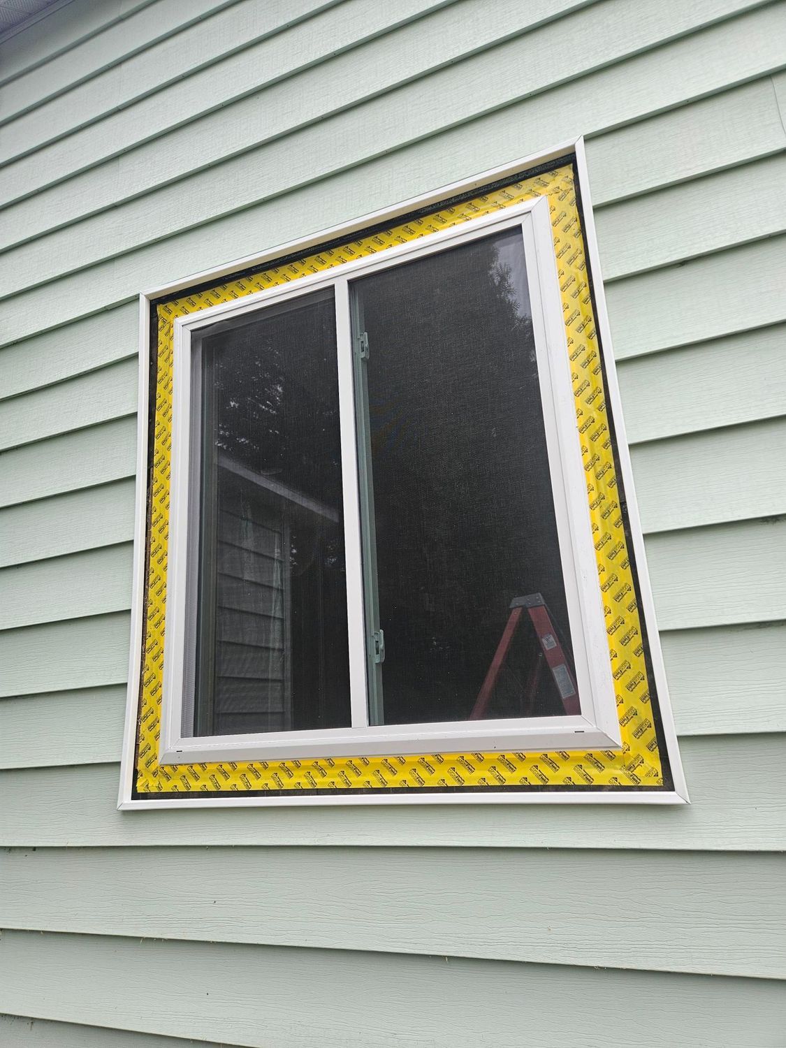 Partially open window with yellow trim on light gray house siding