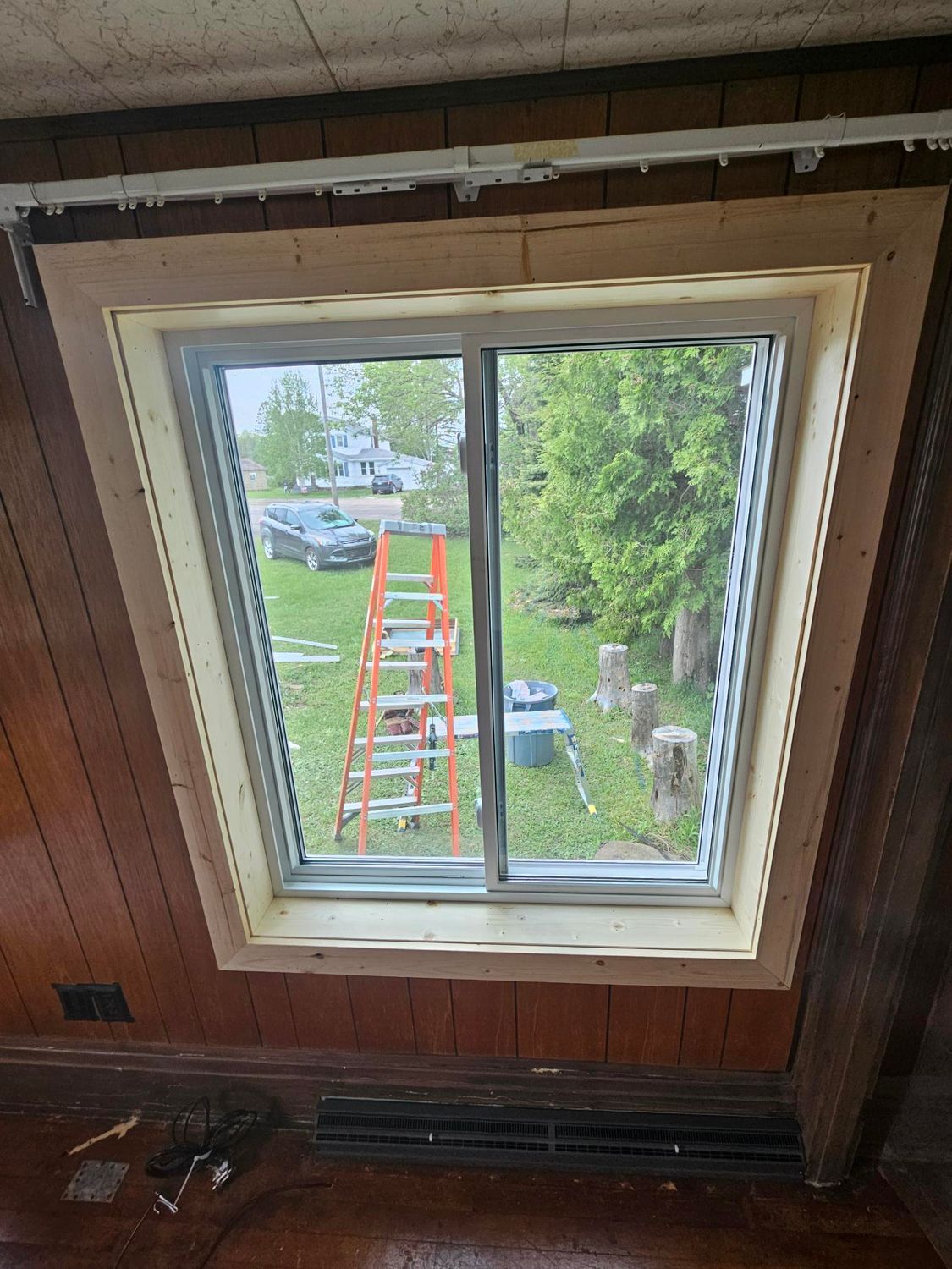 Interior view through a window toward a yard with ladders, trees, and a parked truck.
