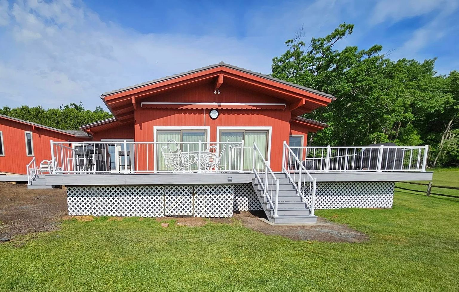 Red house with white deck and stairs on a grassy lawn under a blue sky