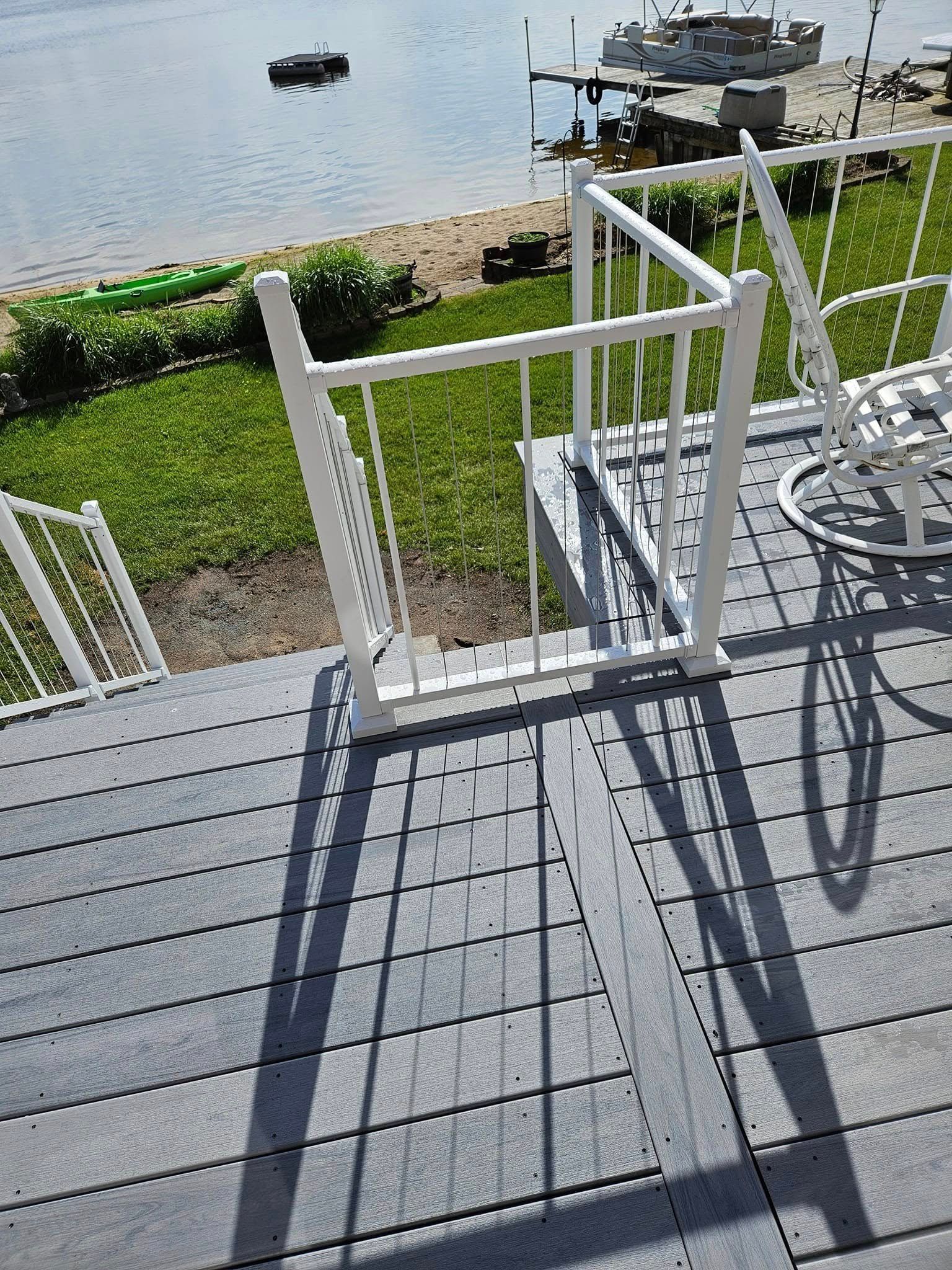Sunny deck overlooking water with white railing, steps, and a bicycle shadow on gray boards