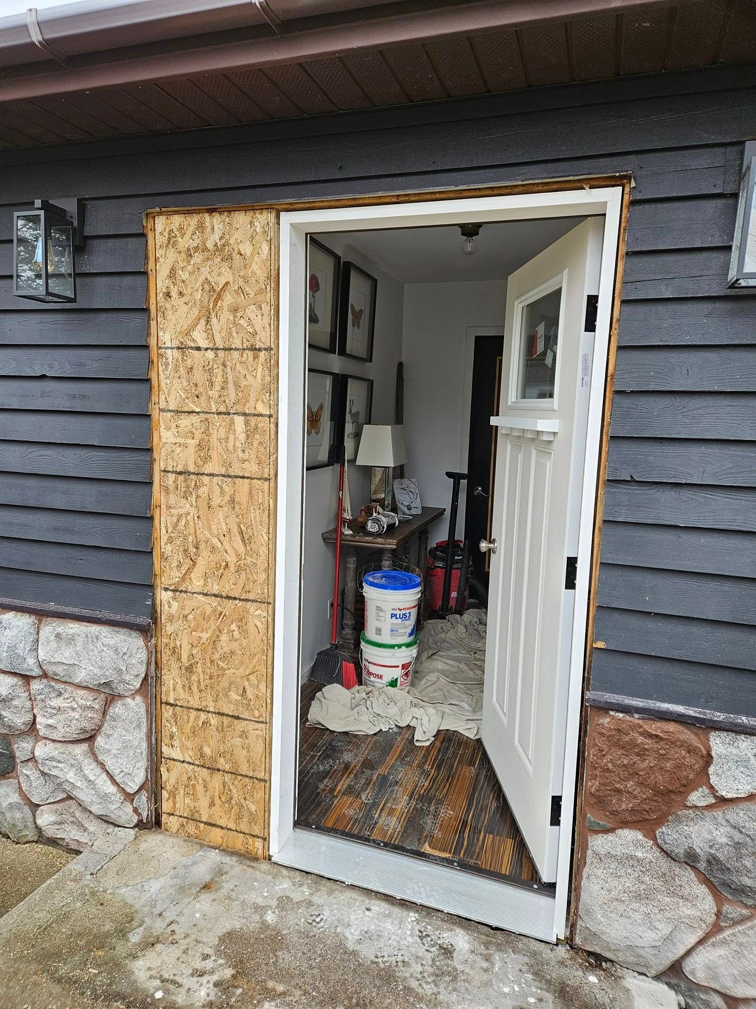Open exterior doorway to a small utility room with tools and supplies inside