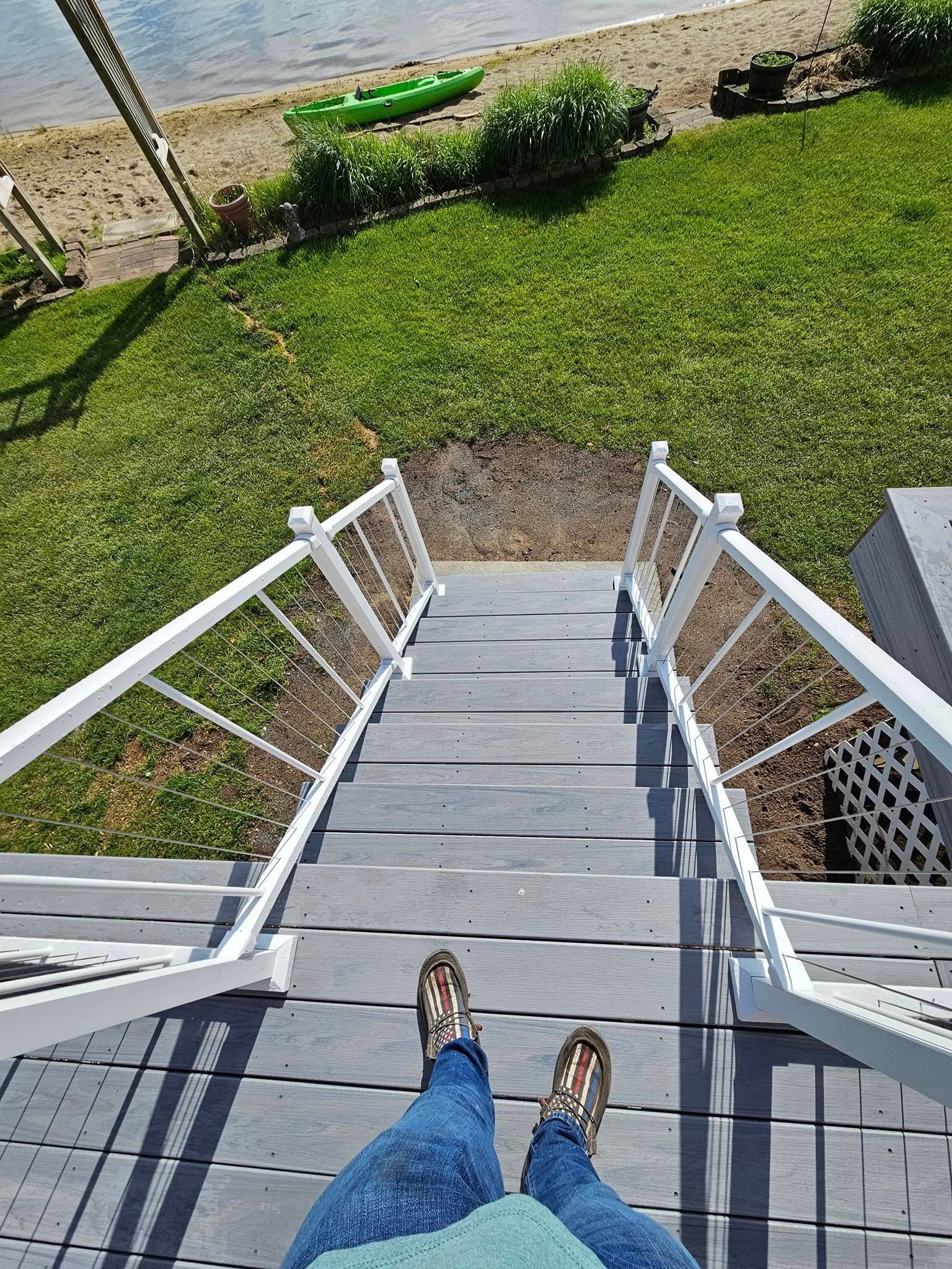 View from top of gray wooden stairs descending to a grassy yard by a waterfront.