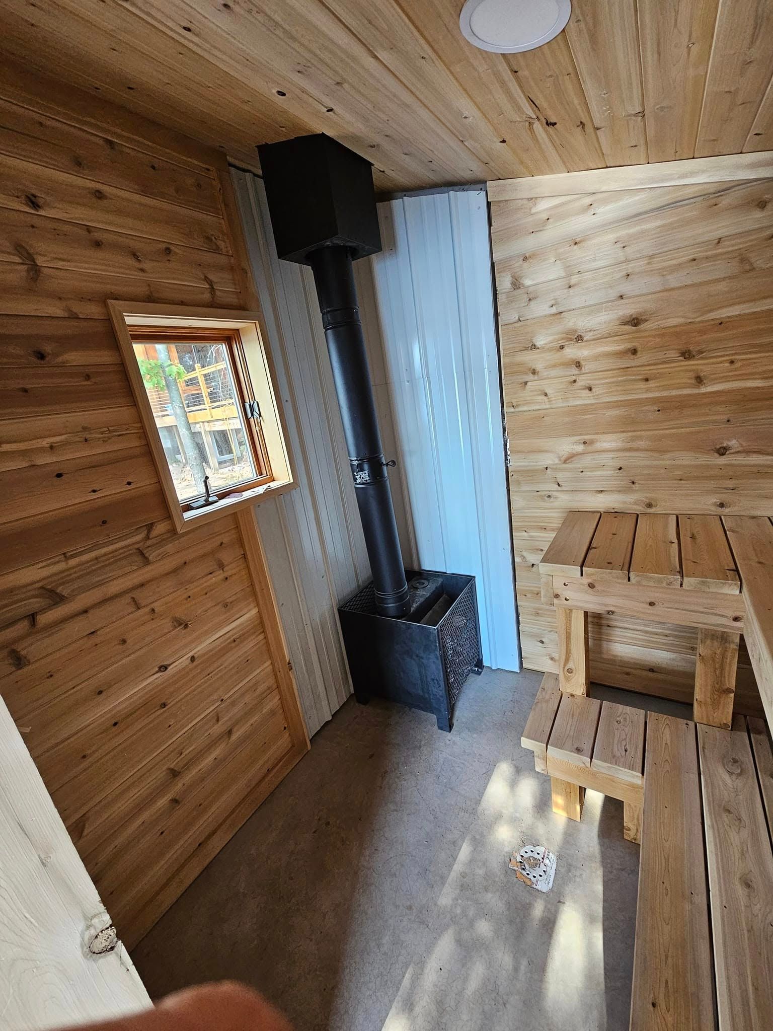 Small wood-paneled cabin interior with a black wood stove, window, and built-in bench seating.