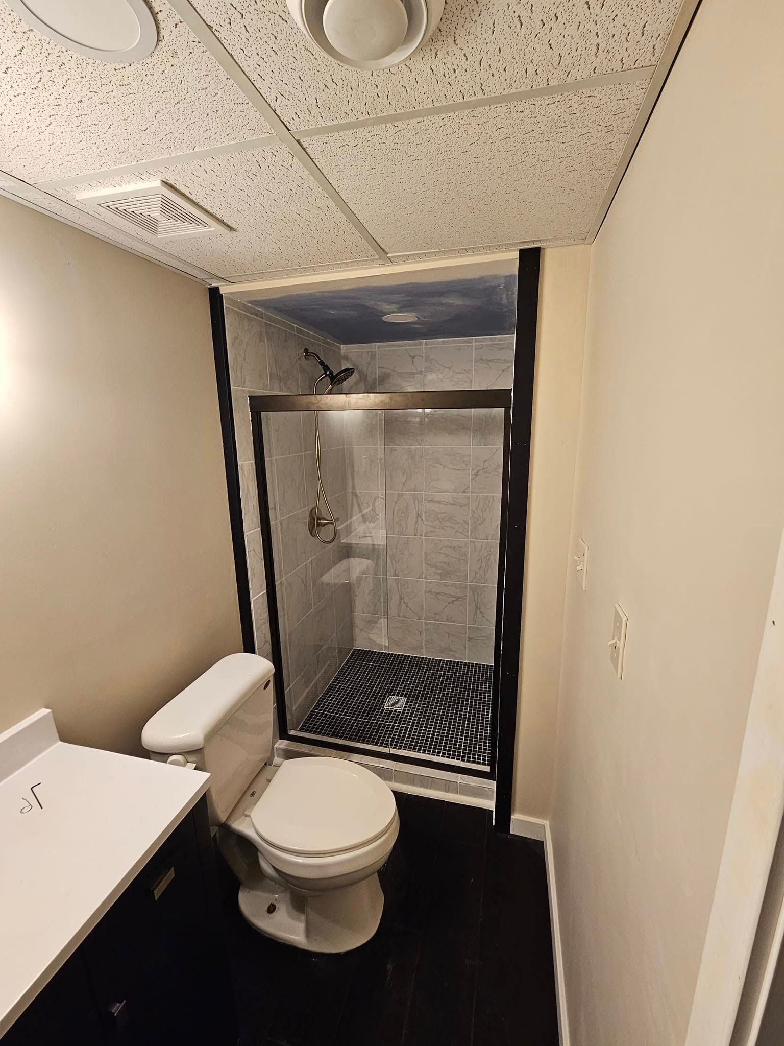 Small bathroom with toilet, sink, and a shower stall with a shower curtain and black floor mat.