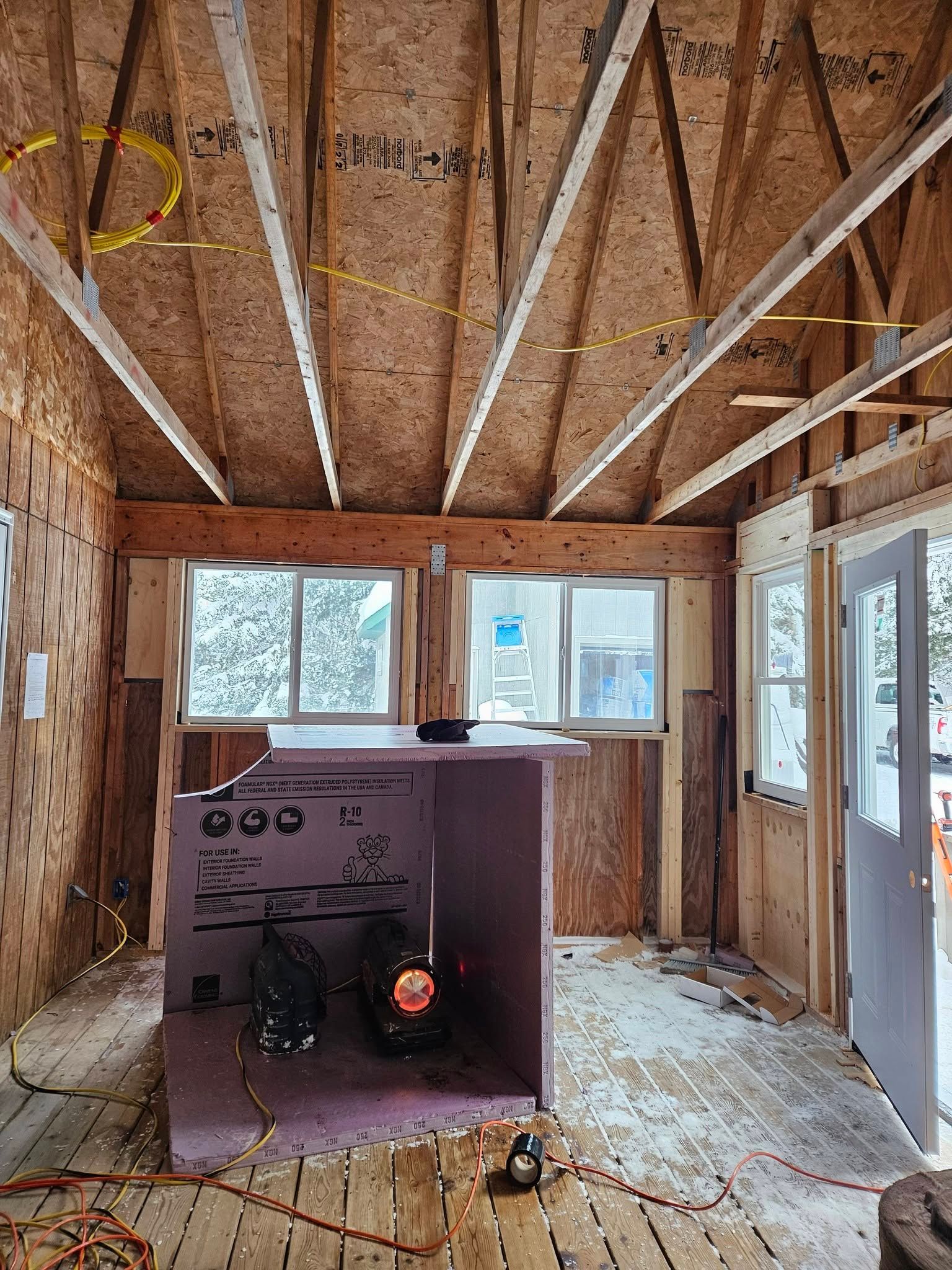Unfinished room with exposed rafters, window openings, and a small wood stove near the back wall.