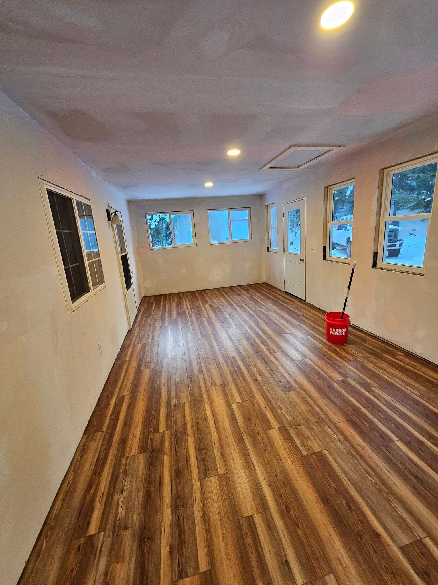 Empty room with wood floors, white walls, ceiling lights, and a red bucket near the right wall.