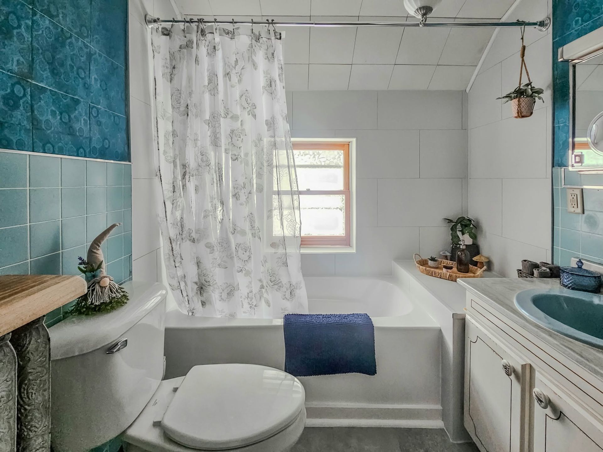 Small bathroom with a toilet, tub, blue tile accents, white vanity, and a shower curtain by a window.