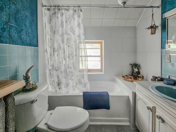 Small bathroom with teal accents, white shower curtain, and sink beside a toilet.