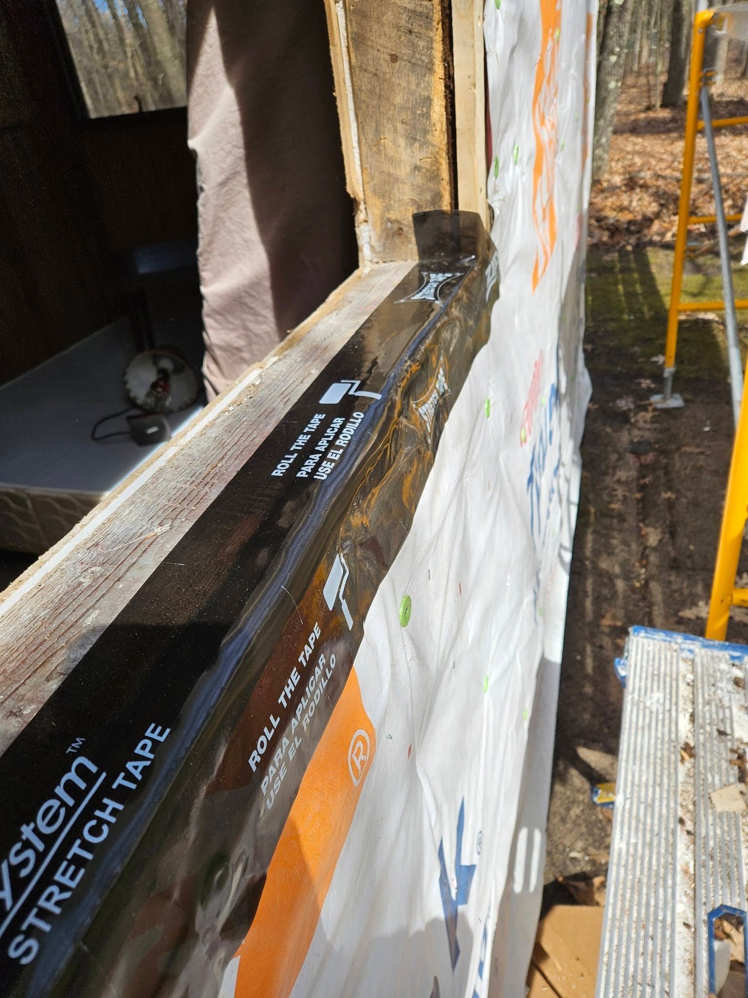 Close-up of a black window sill and white house wrap on a construction site.