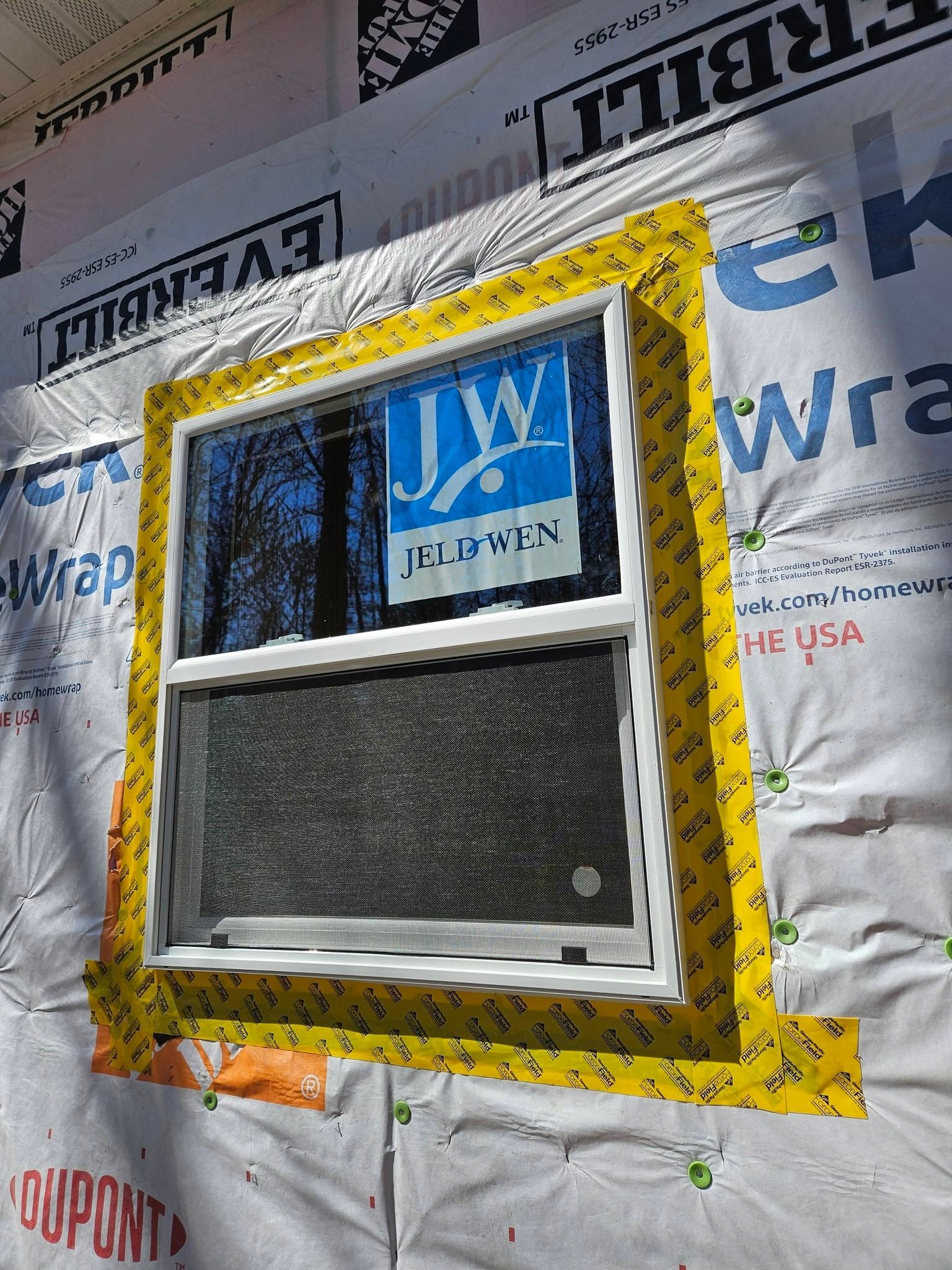 Window framed with yellow flashing on house wrap under construction