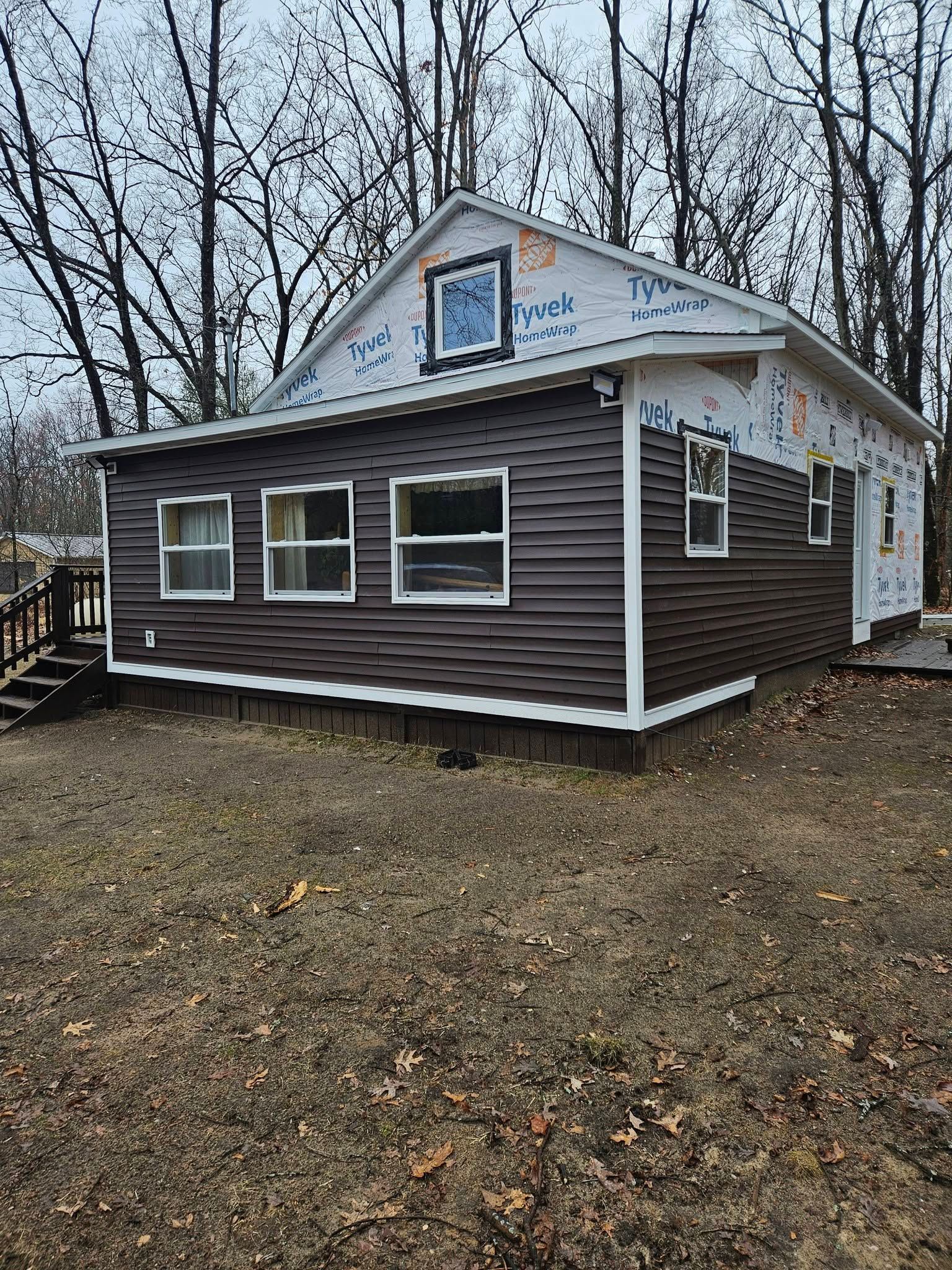 Small brown house with white trim, three front windows, and bare trees in a yard.