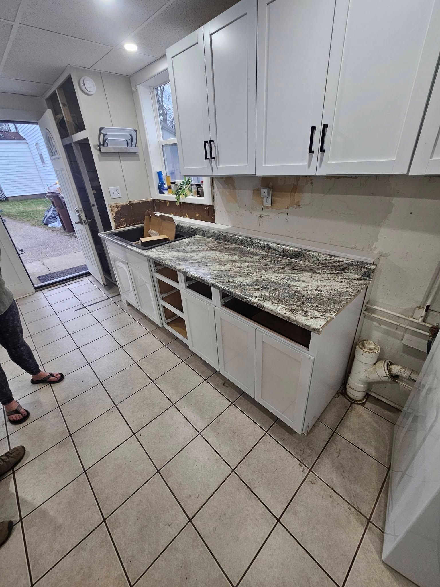 Kitchen with white cabinets, granite countertop, tiled floor, and one open cabinet under renovation.