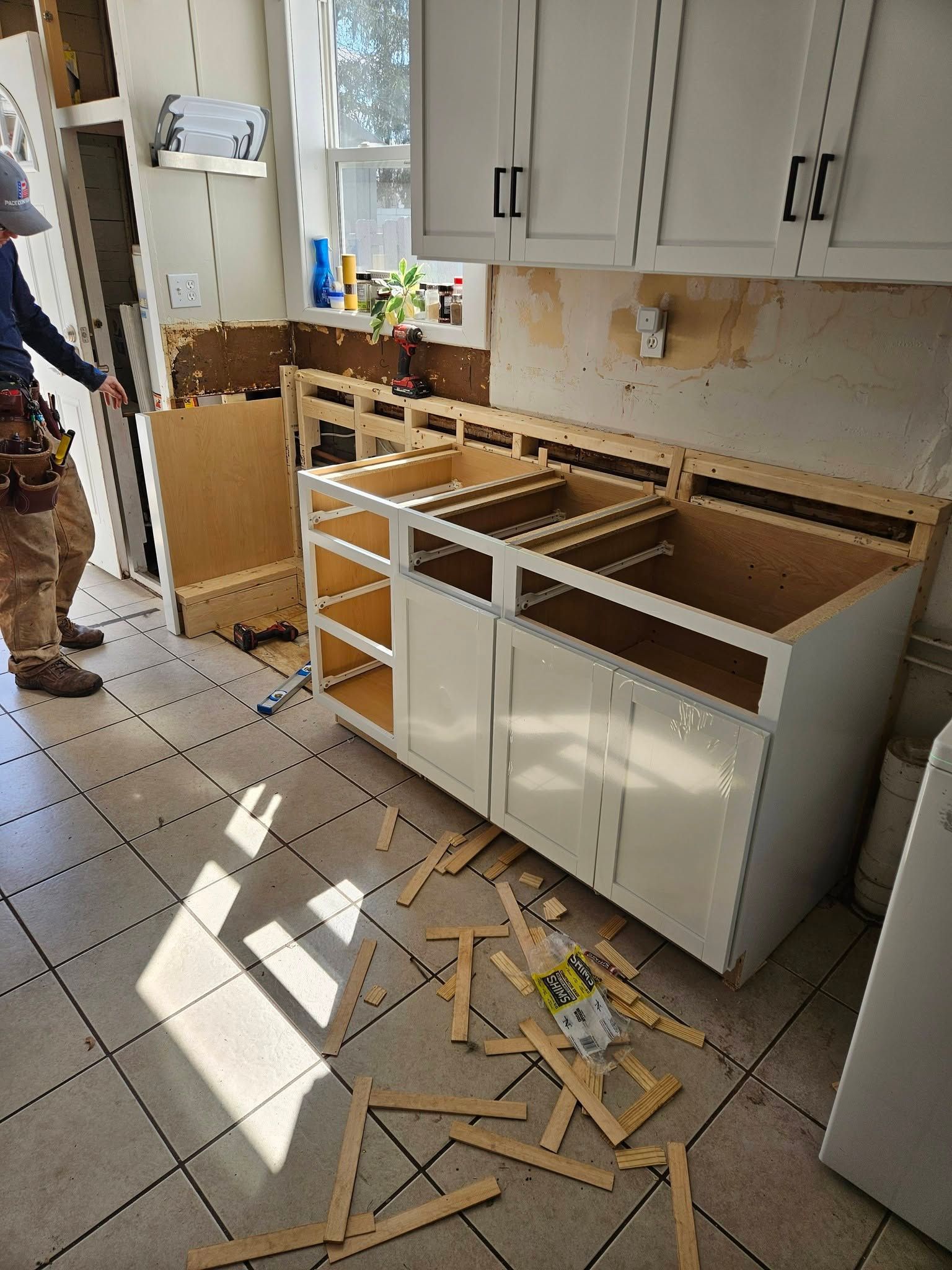 Damaged kitchen cabinets and drawers overturned, with broken wood scattered on the tiled floor.