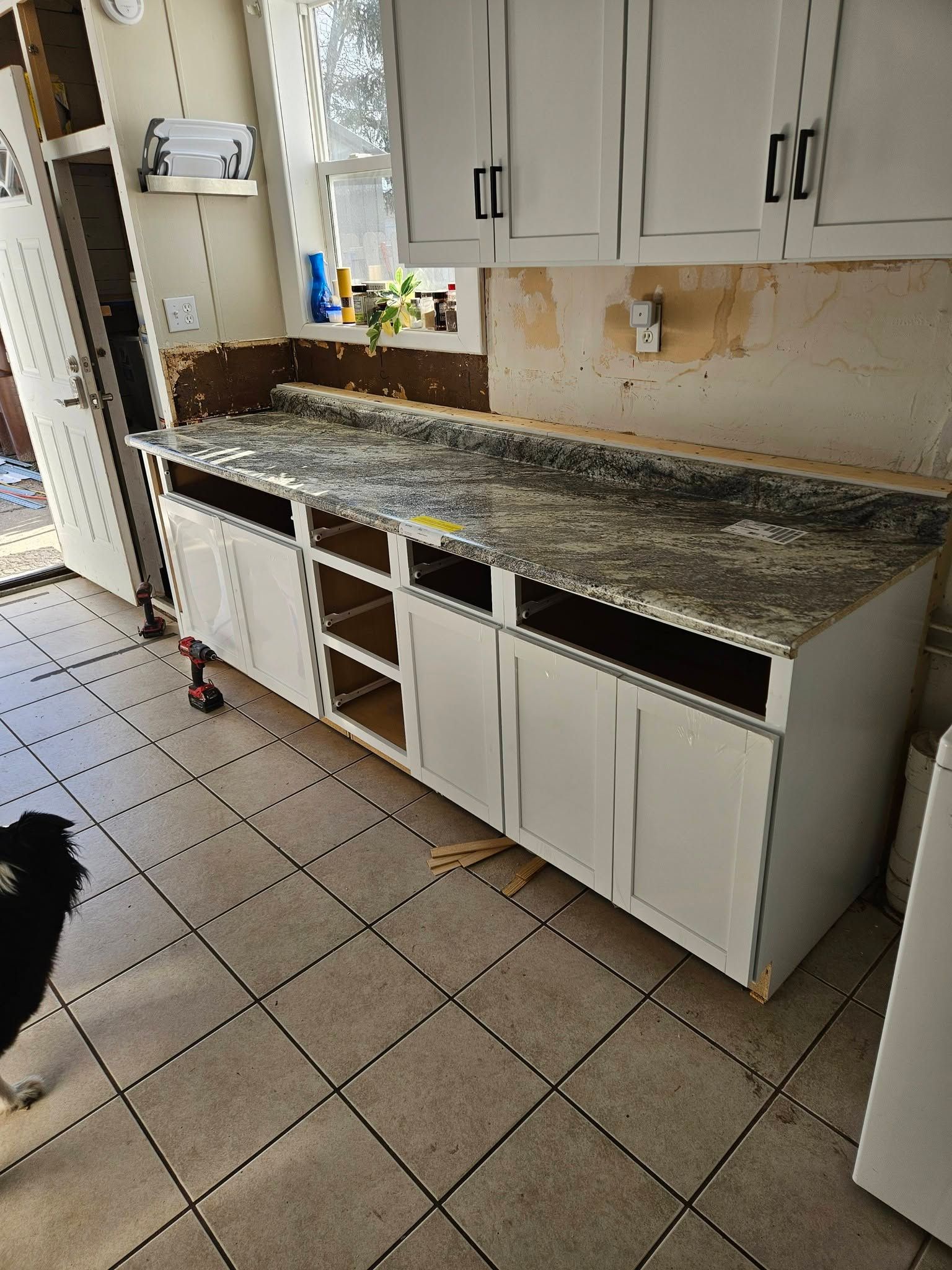 Damaged kitchen with torn-off cabinet doors, exposed wall, and debris on the countertop and floor
