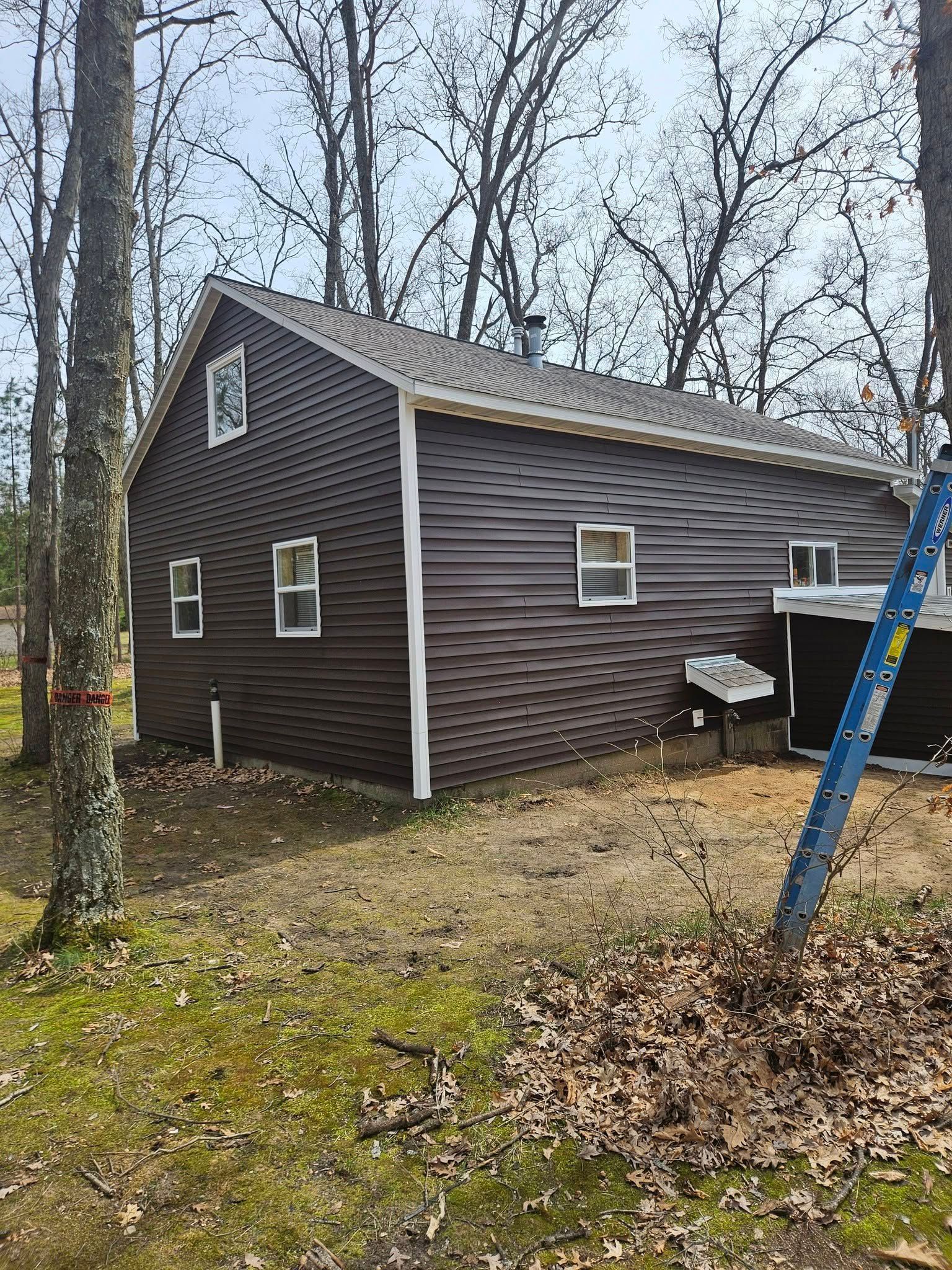 Small brown house with white trim among leafless trees, with a blue ladder in the foreground.