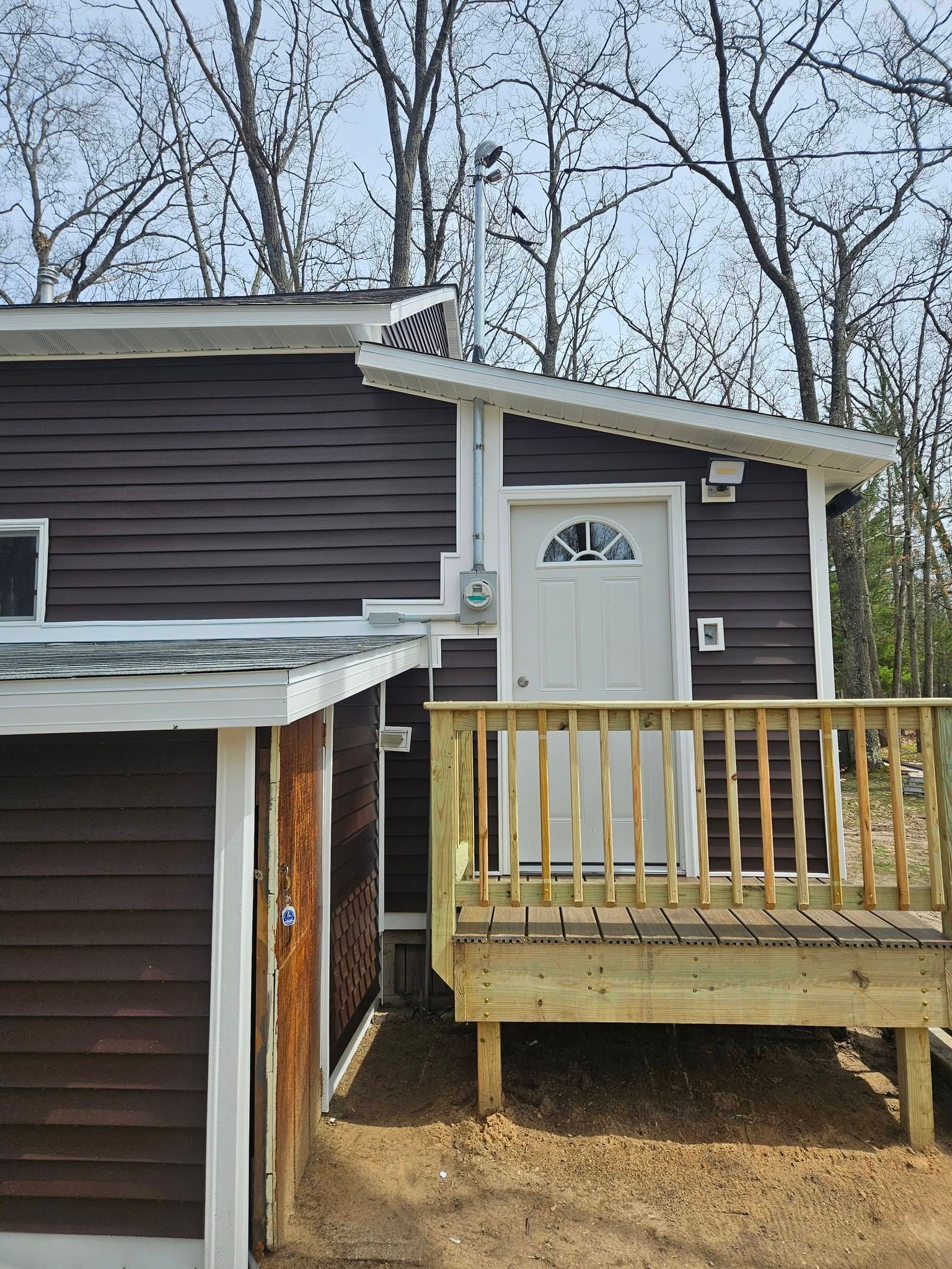 Small brown house exterior with a white door and a wooden porch railing under bare trees.