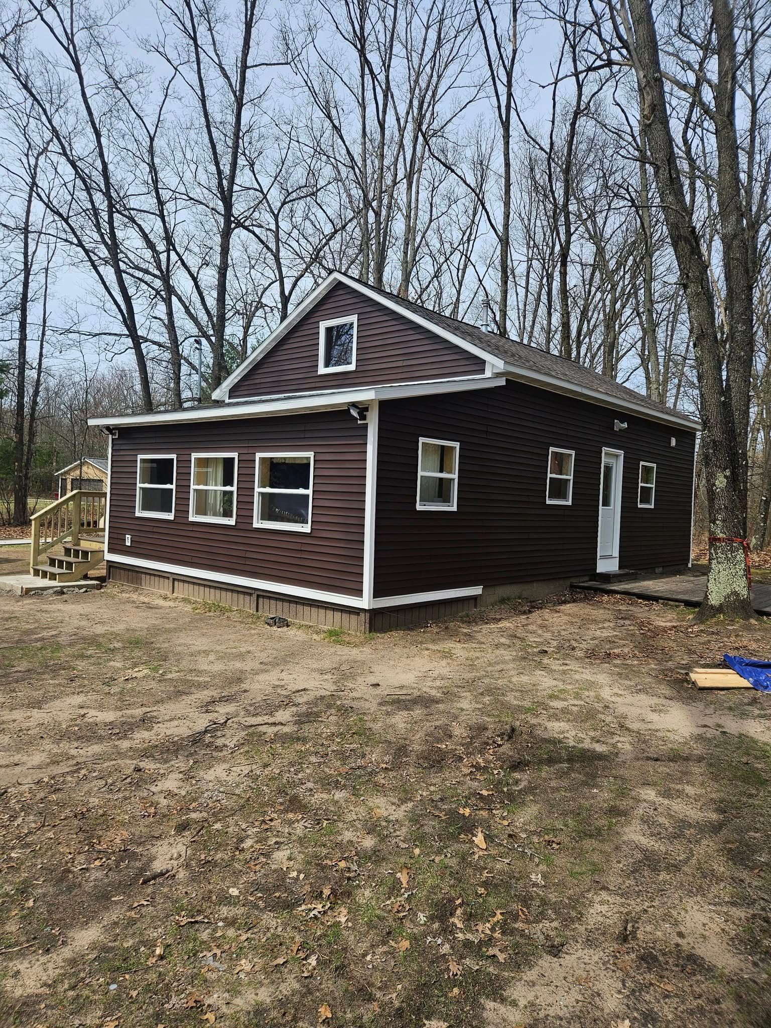 Small brown cabin with white trim in a leafless wooded yard