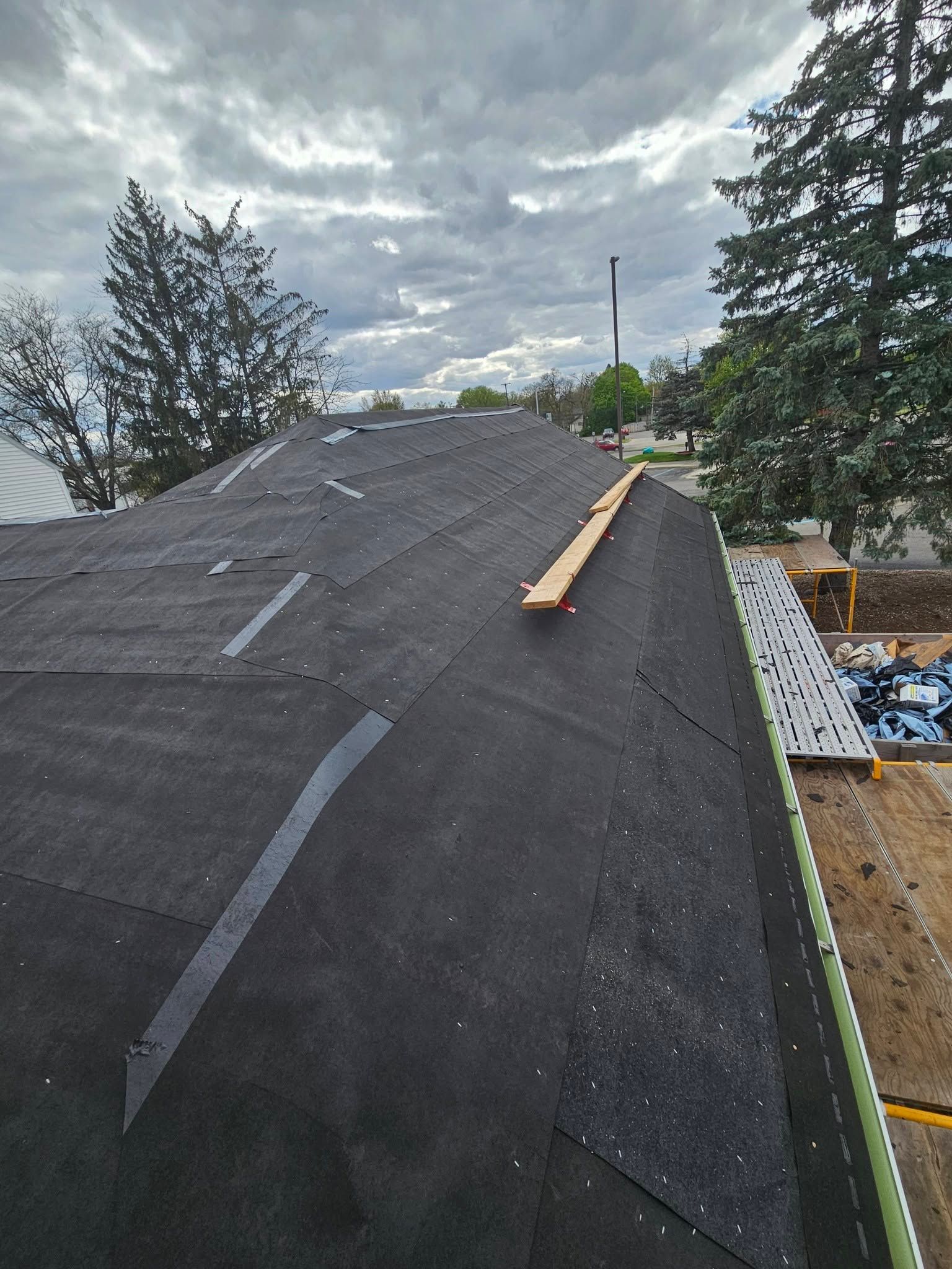Roof under repair with new underlayment and a wooden plank on top under cloudy sky