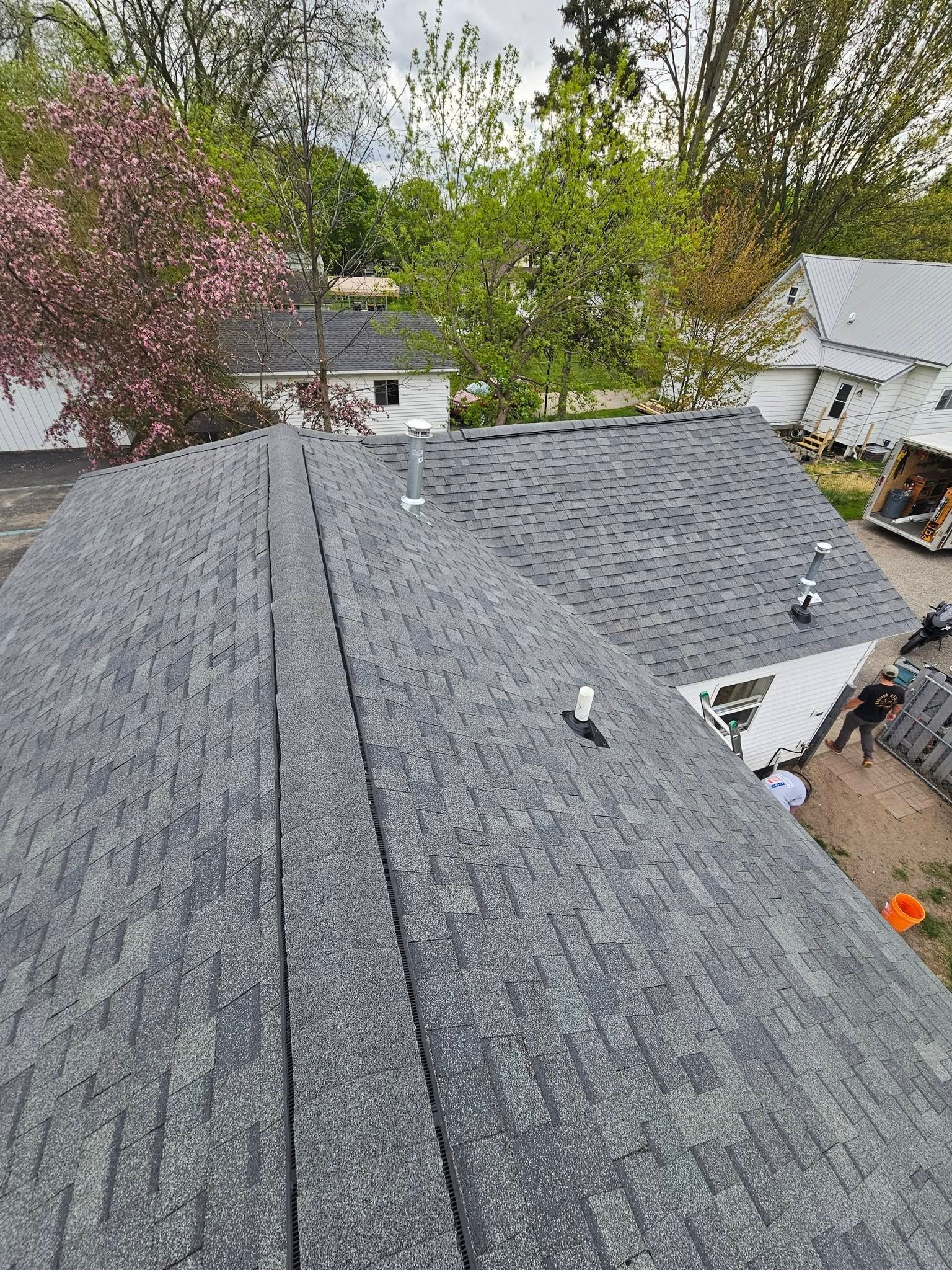 Rooftop with gray shingles, surrounded by trees and neighboring houses, under an overcast sky