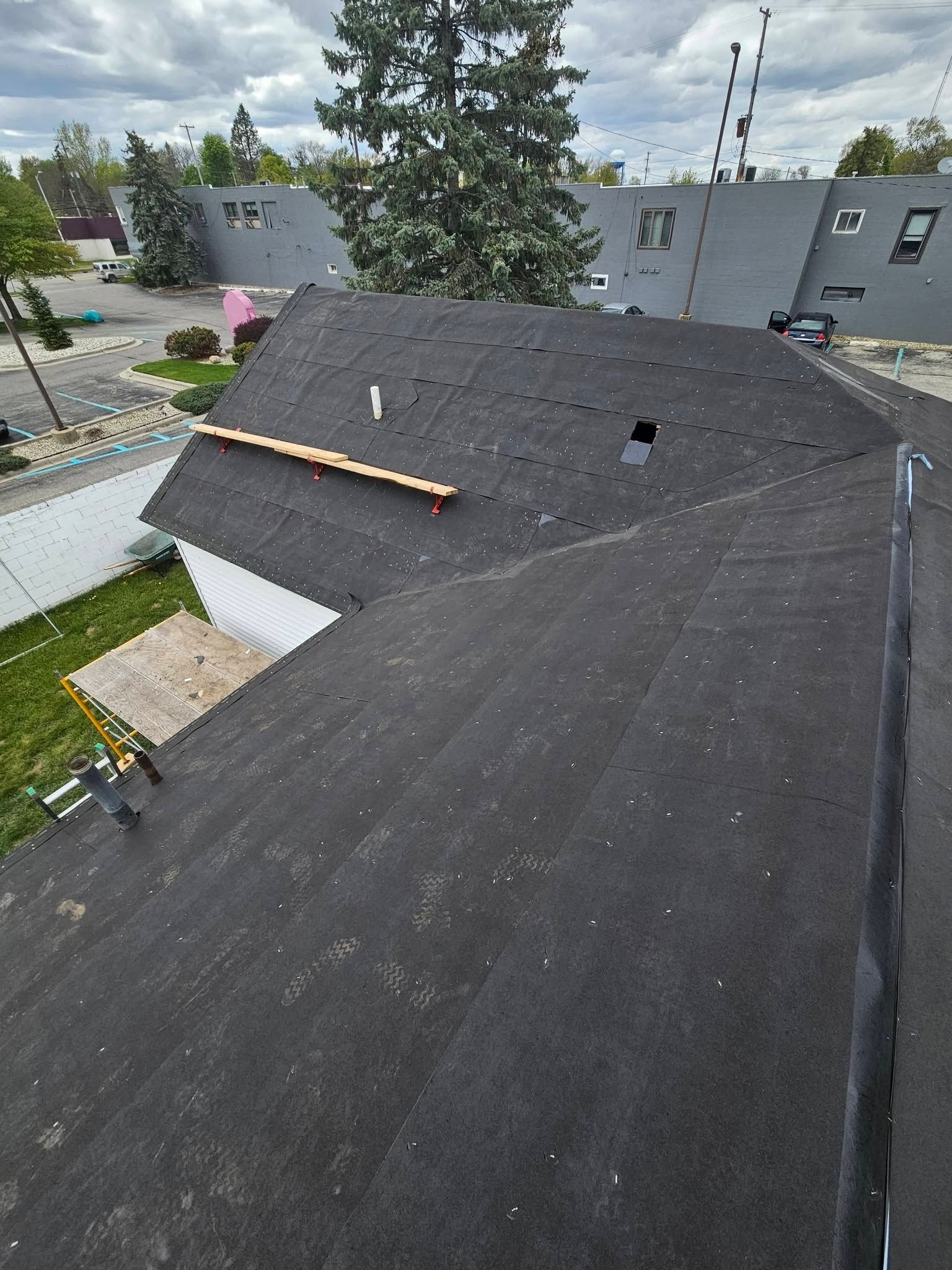 Aerial view of a dark shingled rooftop with neighboring houses and trees nearby