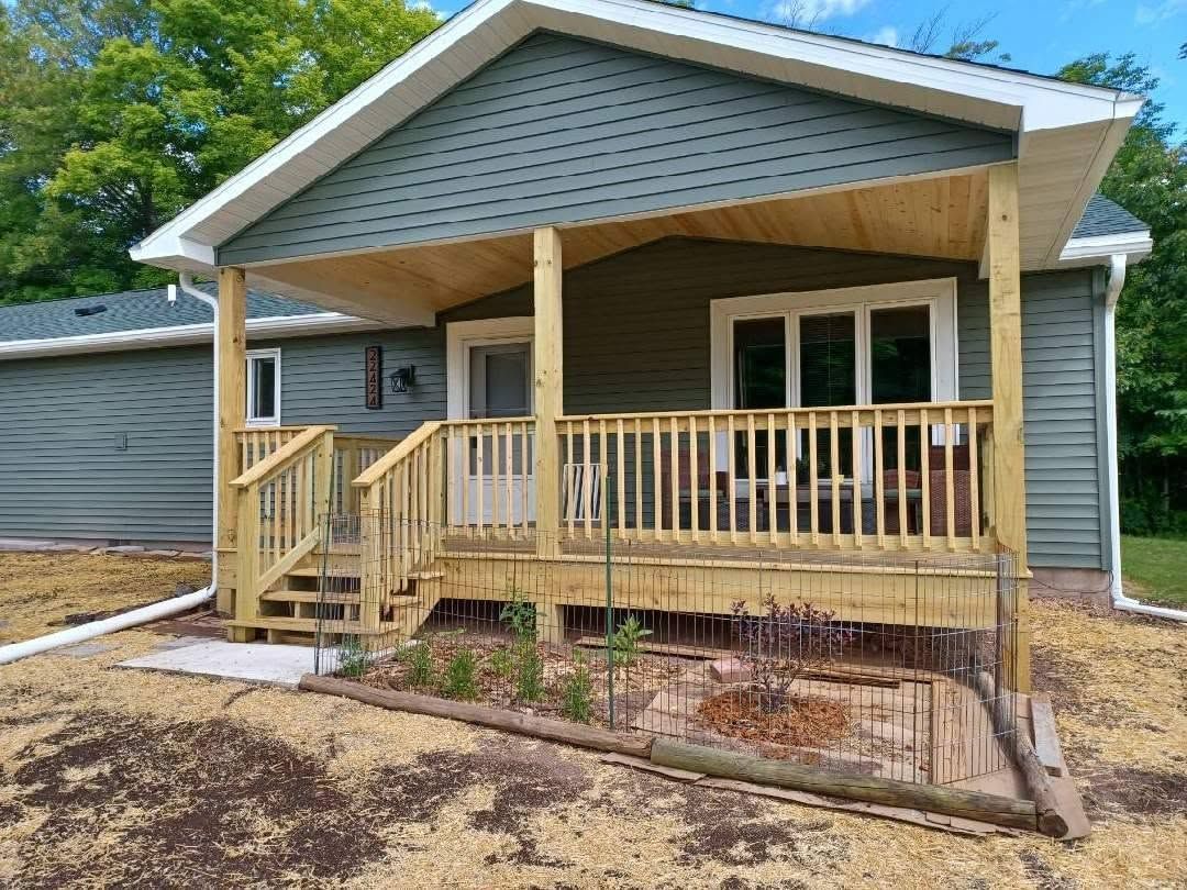 Front porch of a gray house with wood railing, steps, and covered roof
