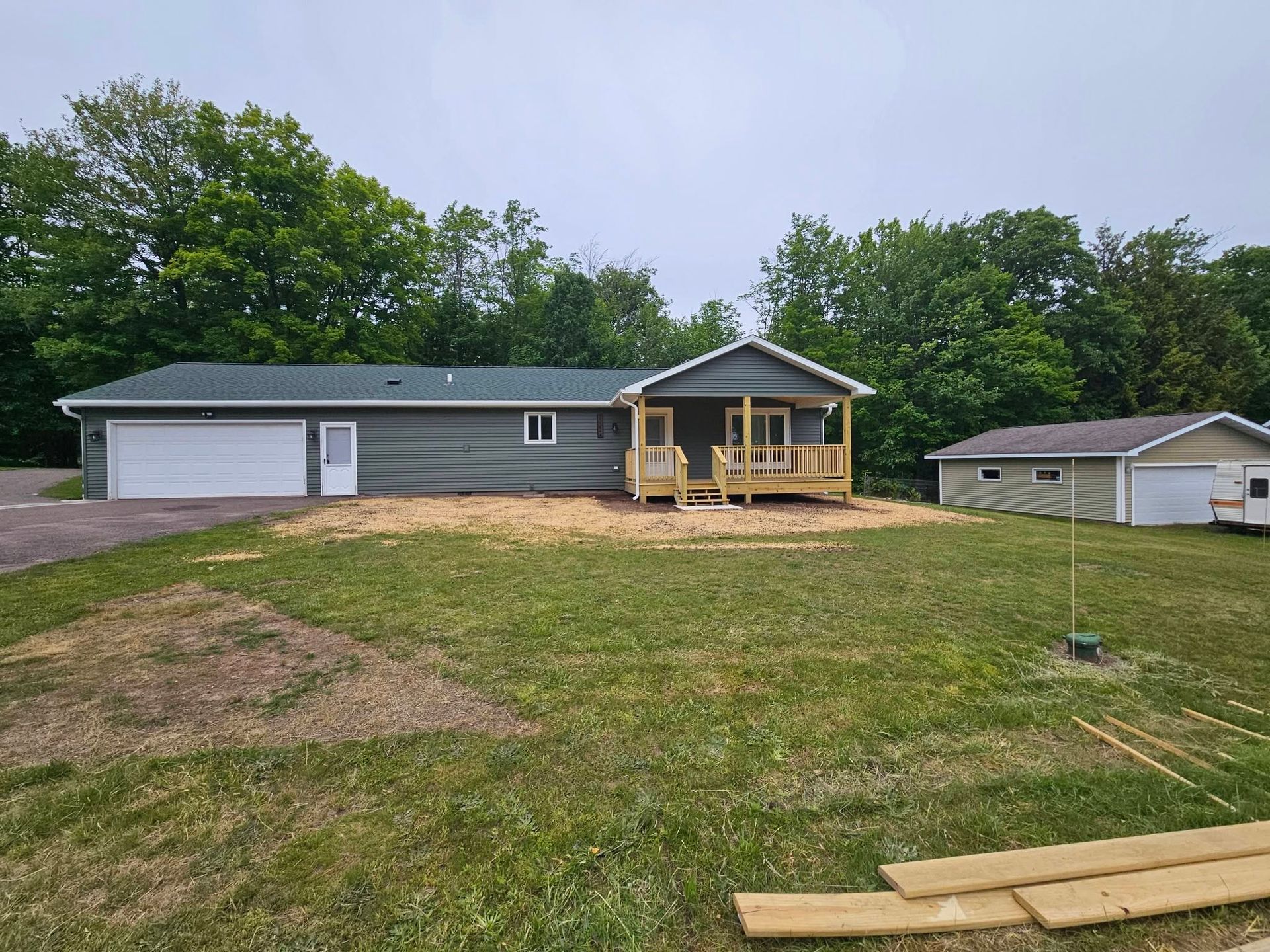 Single-story gray house with white garage, front porch, and a large grassy yard under cloudy skies