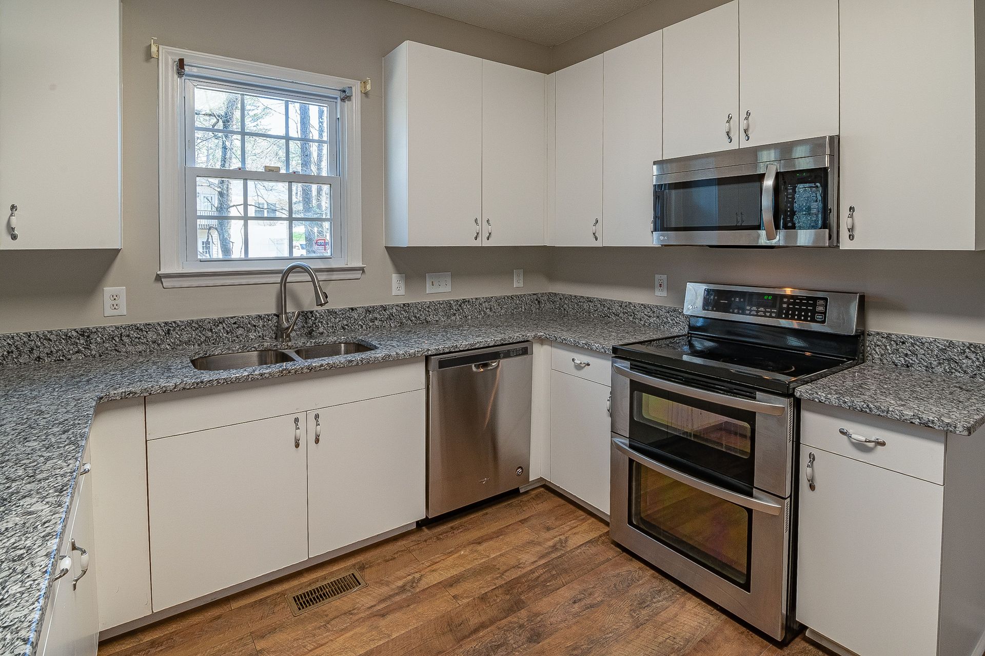 Modern kitchen with white cabinets, granite countertops, stainless steel appliances, and a window above the sink