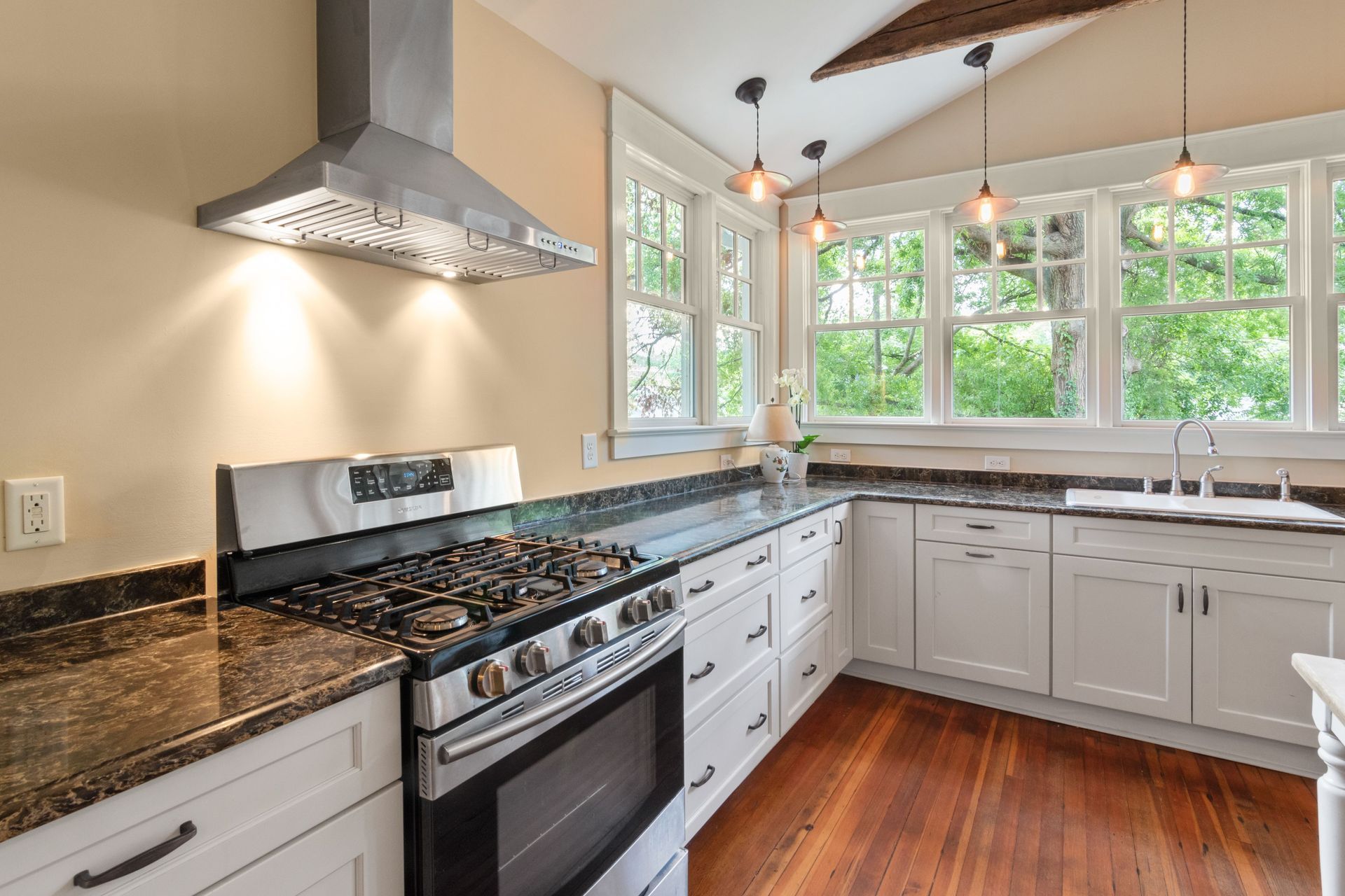 Bright kitchen with stainless stove, granite counters, white cabinets, and large windows looking out to trees