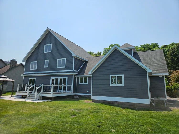 Gray house with white trim, porch, and lawn under a clear blue sky