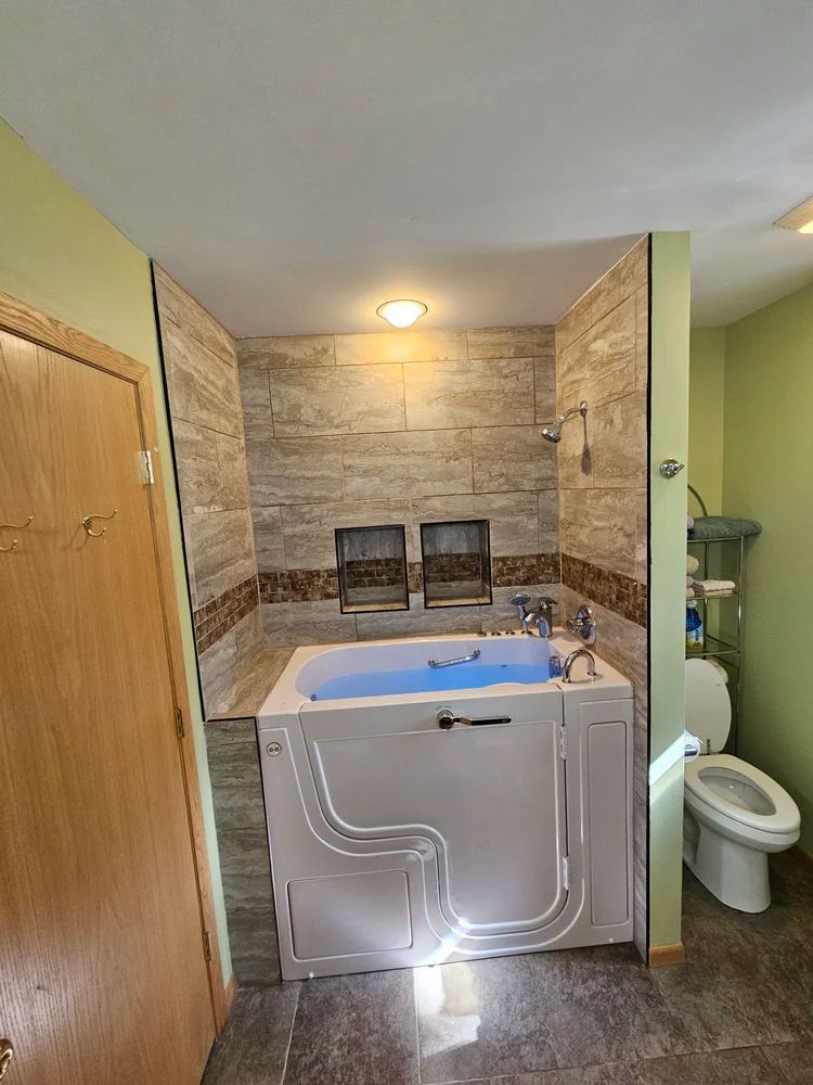 Bathroom with a walk-in tub, tiled shower wall, and toilet beside it.