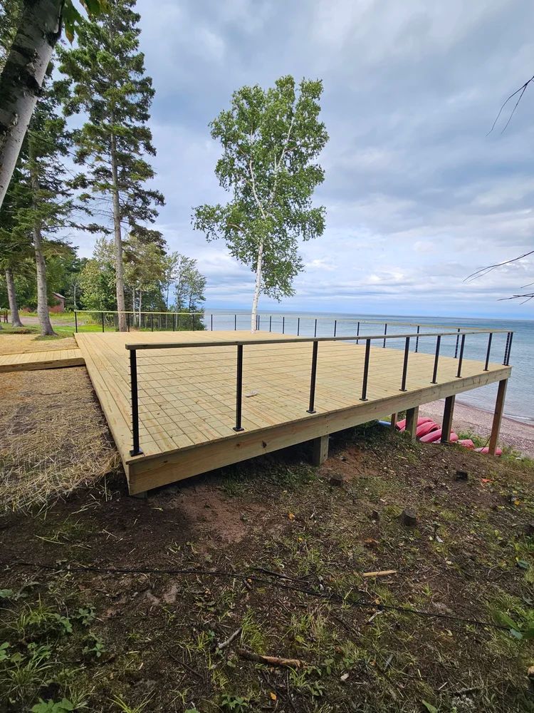 Small wooden deck overlooking a lake, with trees and a cloudy sky in the background.