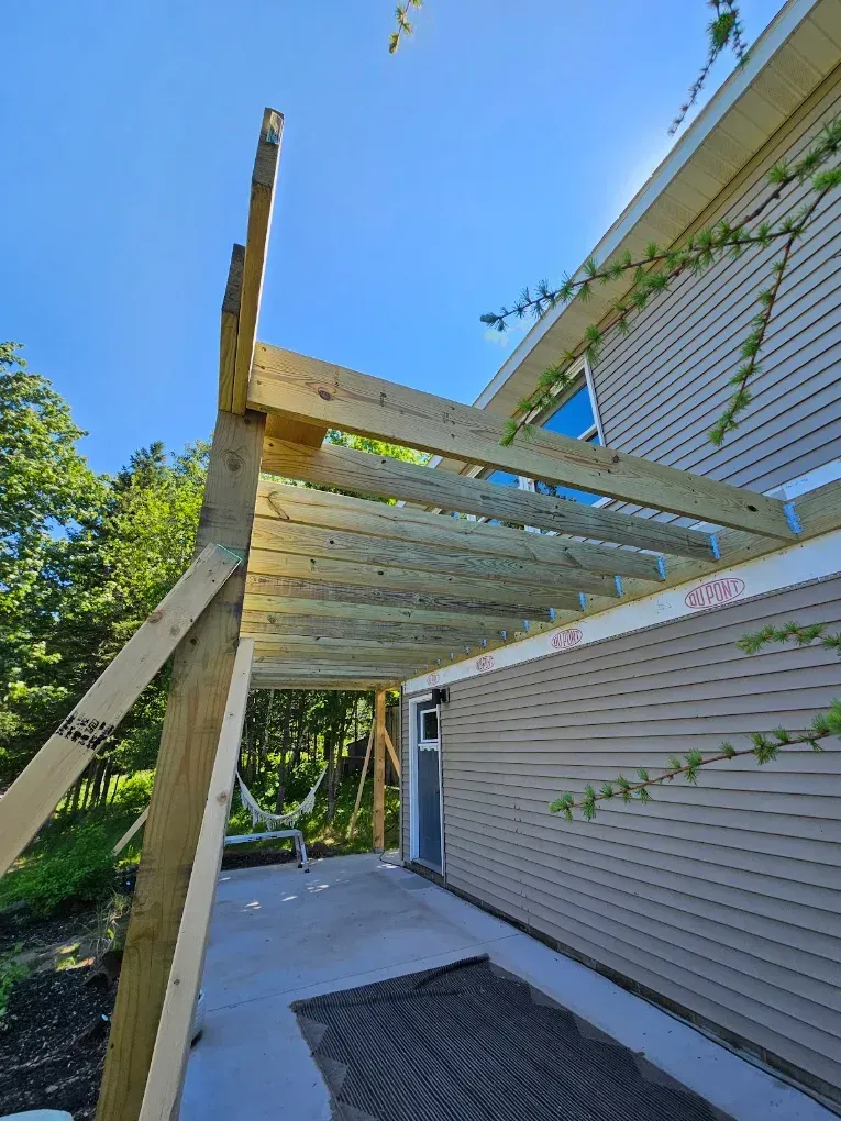 Backyard pergola under construction beside a white-sided house on a sunny day