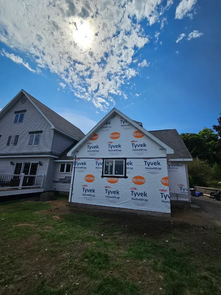 House under construction wrapped in white Tyvek house wrap under a bright cloudy sky