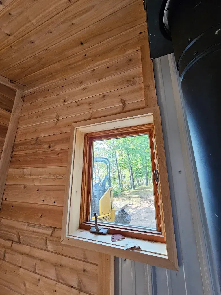 Wood-paneled room with a small window showing a wooded outdoor scene and yellow equipment outside.