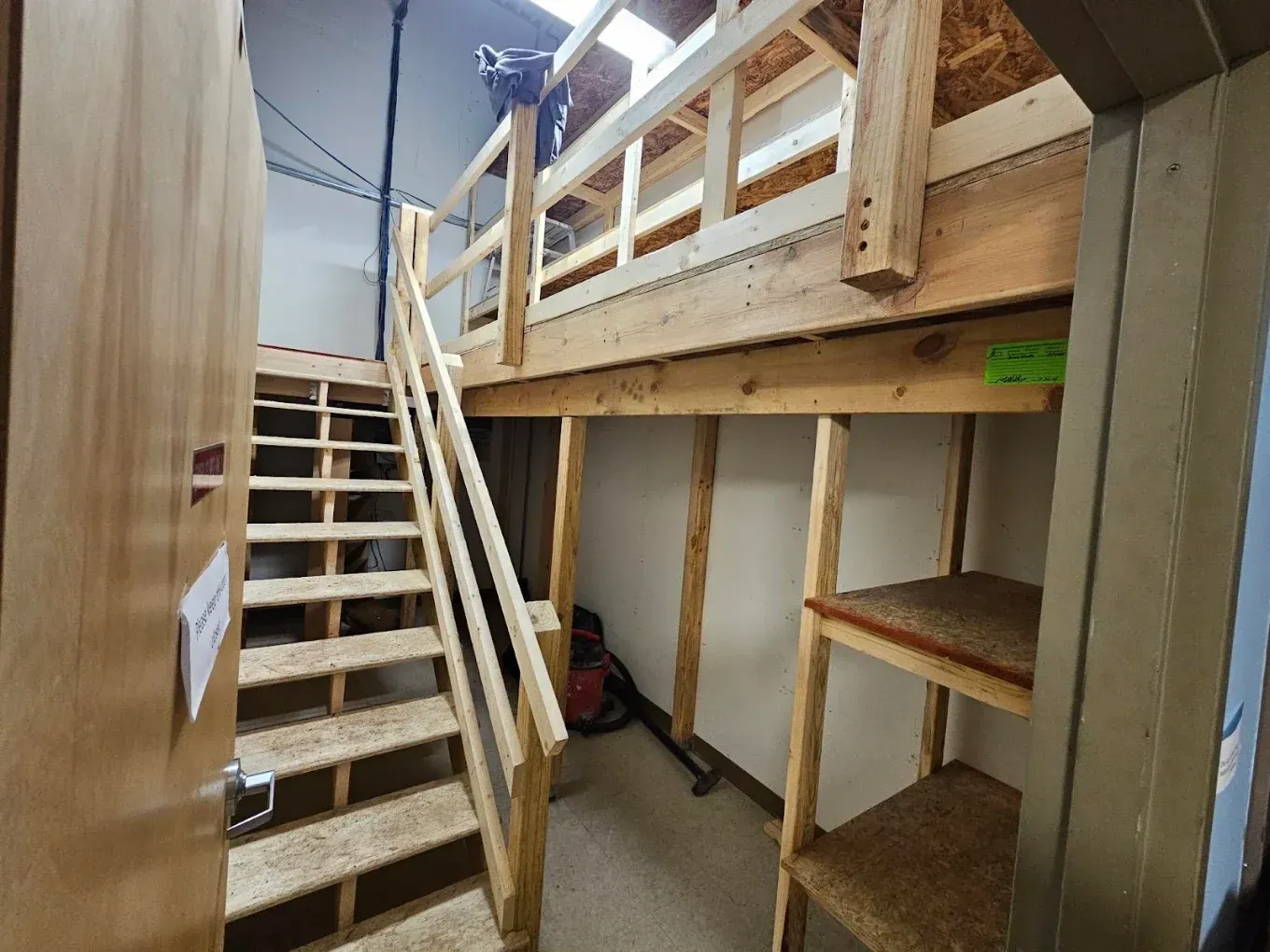 Interior of a lofted bunk bed with stairs, wood railings, and built-in shelving in a narrow room