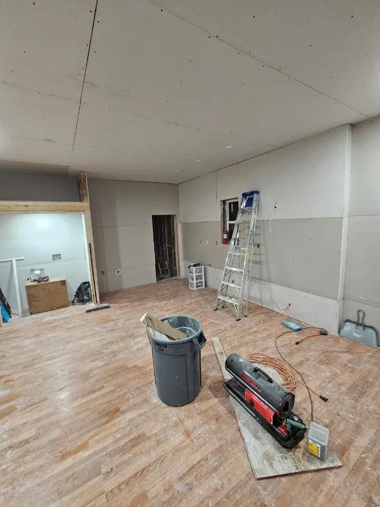 Renovation in progress in a bare room with ladders, tools, and dust on the floor