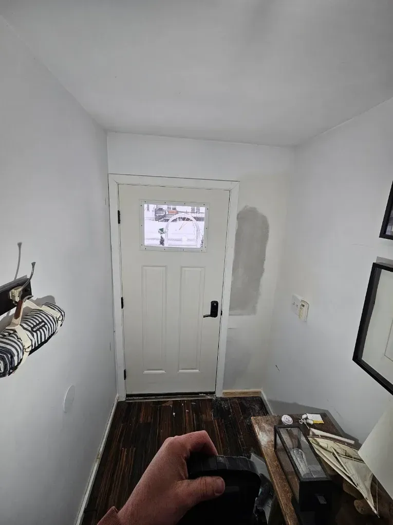 Small hallway entryway with white front door, patch on wall, and a mirror leaning on the right.